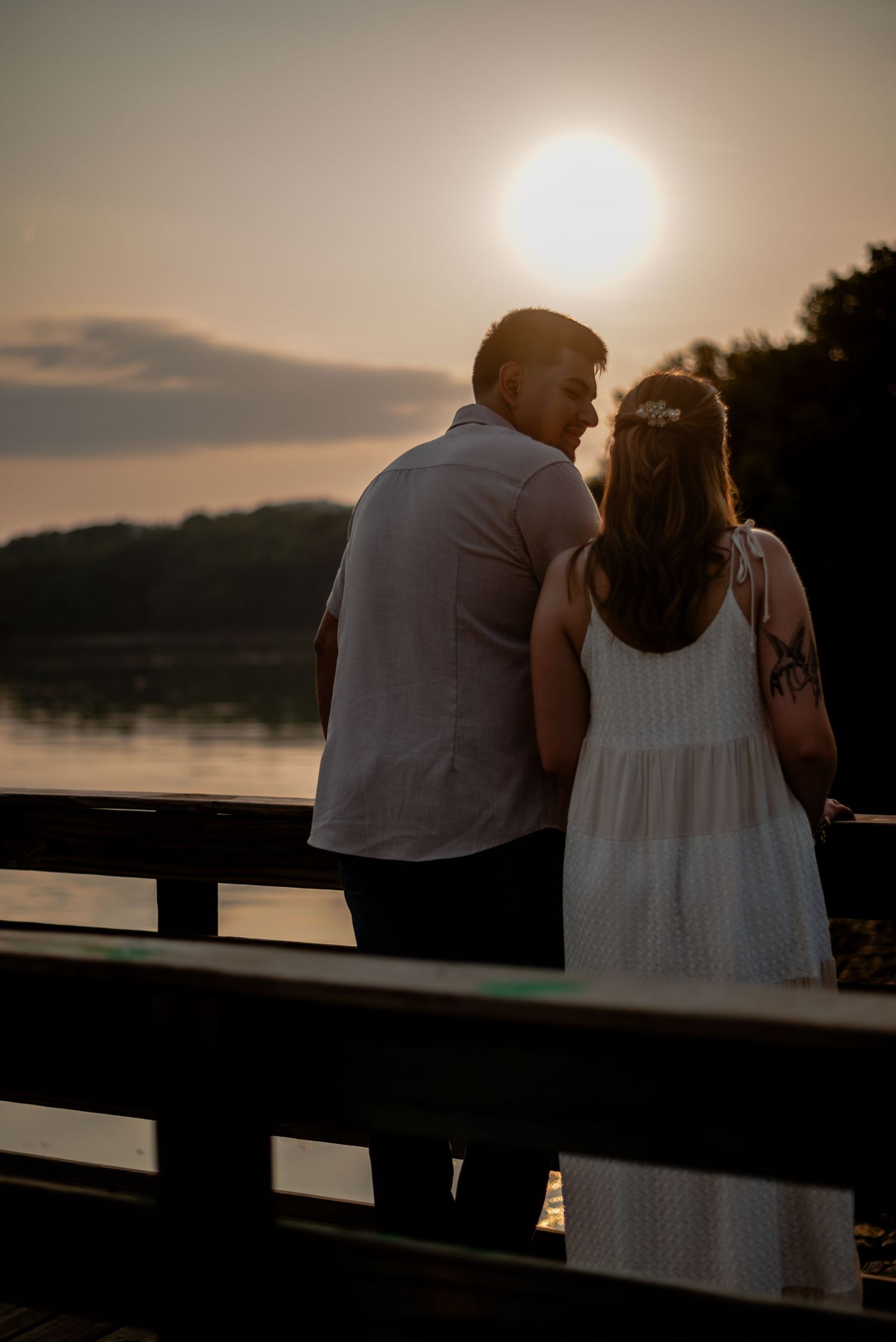 A couple shares a tender moment while watching the sunset from a wooden dock.