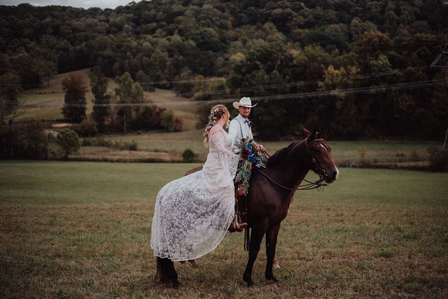 A romantic countryside wedding photo featuring a couple on horseback in a meadow.