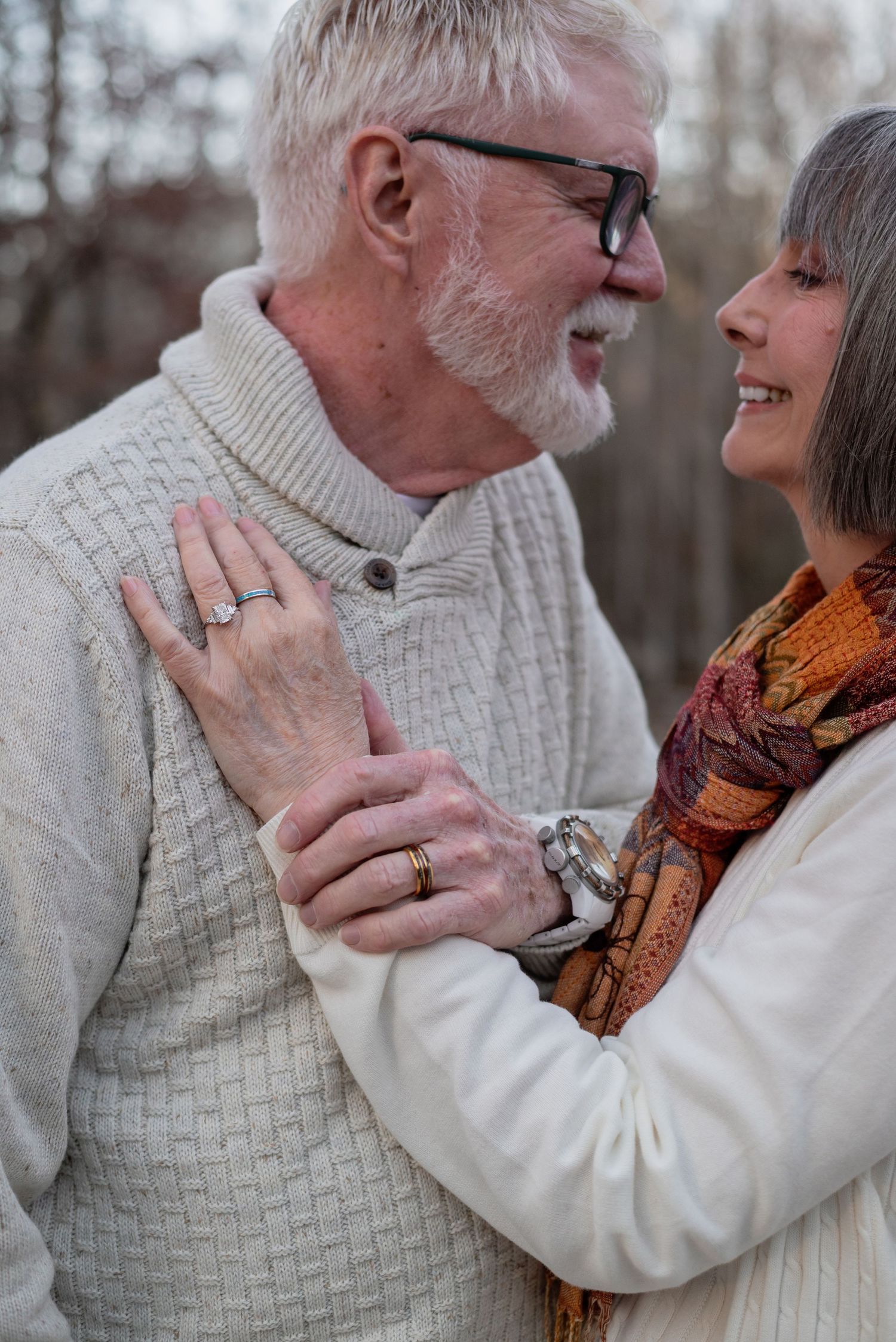 Tender moment between mature couple in cream sweater and autumn scarf outdoors.