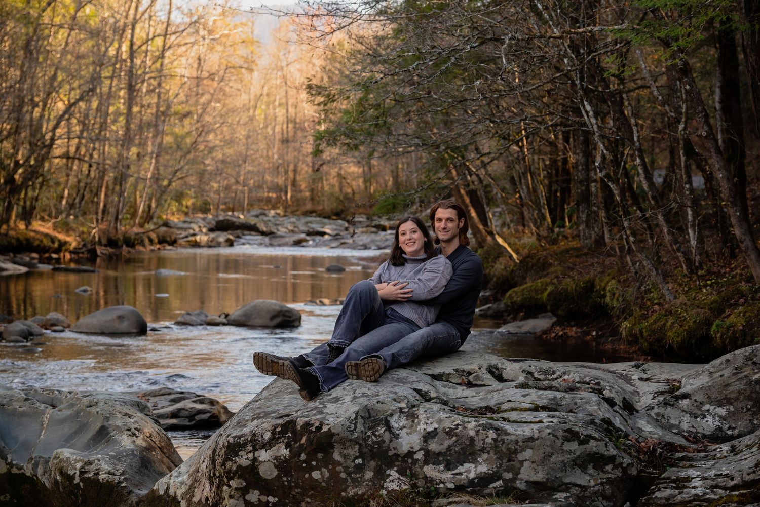 Couple sitting together on rocky outcrop surrounded by autumn forest.