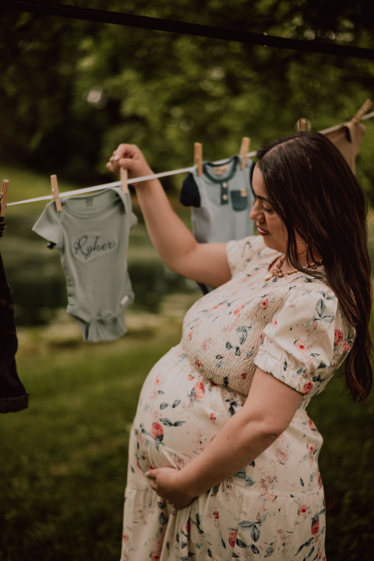 Woman hanging tiny clothes on outdoor clothesline during maternity photoshoot.