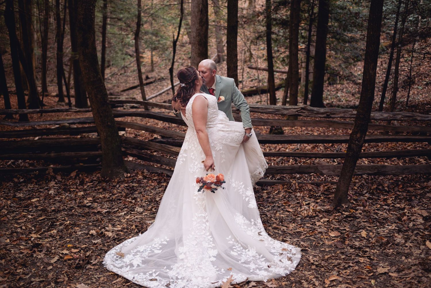 Wedding couple in a forest setting with flowing white lace dress and autumn leaves.