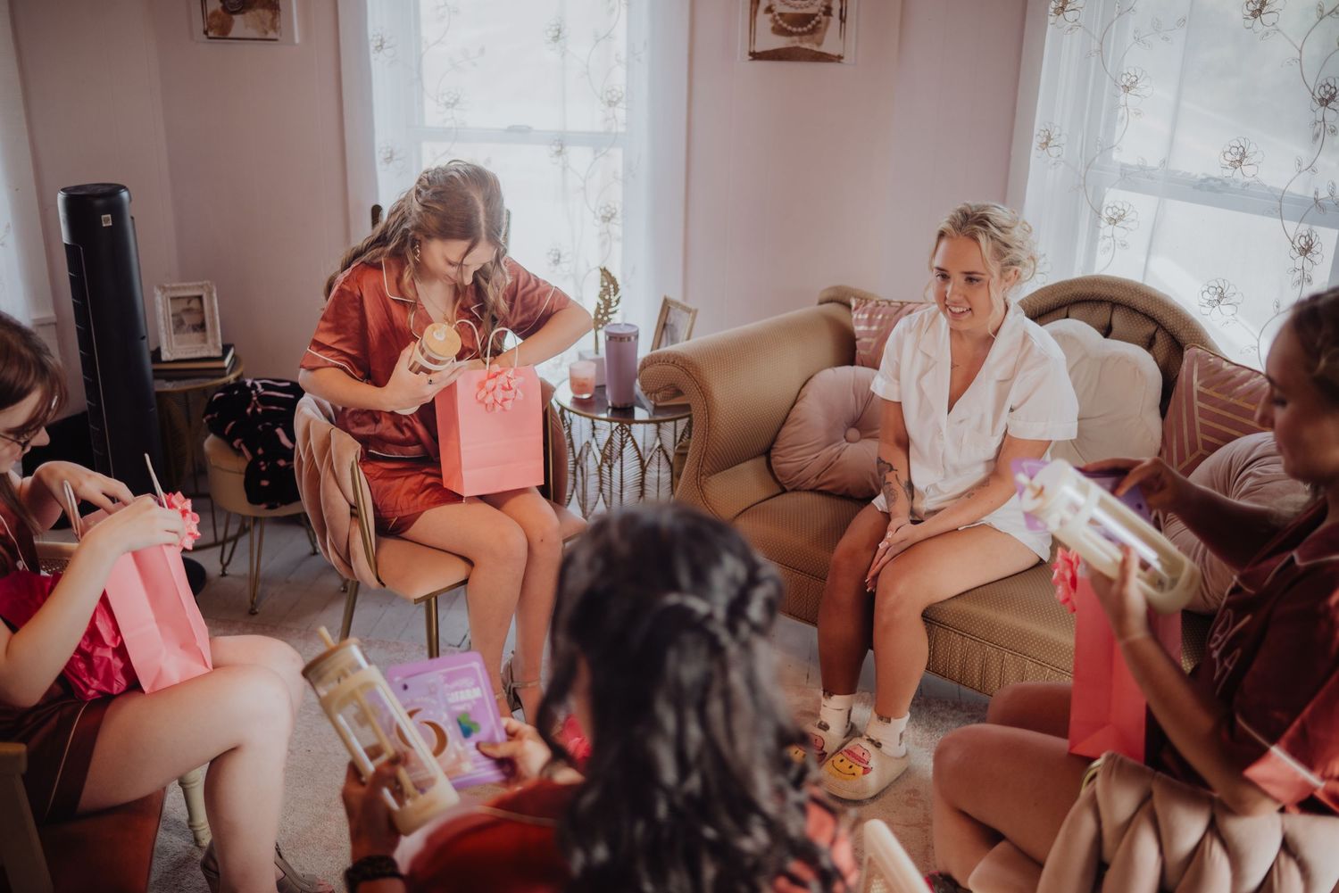 Bridesmaids exchanging gifts during a bridal party getting ready session in a cozy living room.