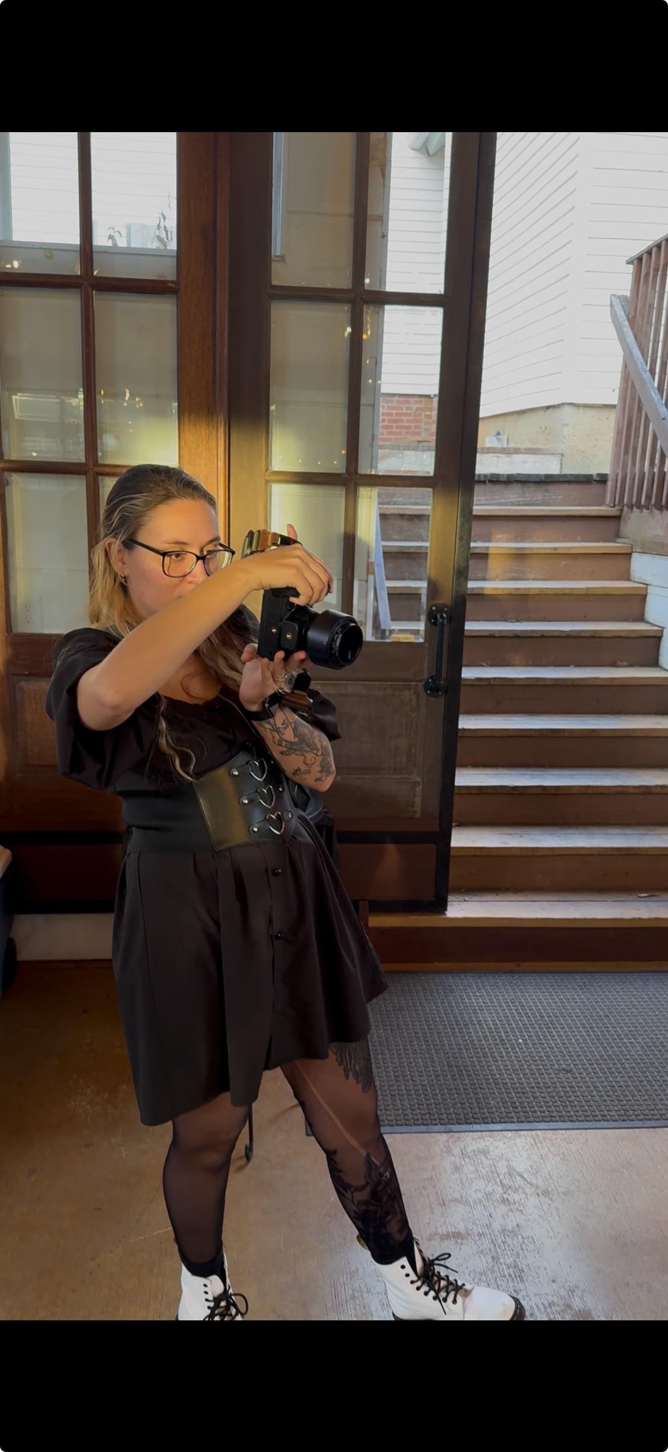 Photographer in black outfit taking photos in indoor venue with glass windows.