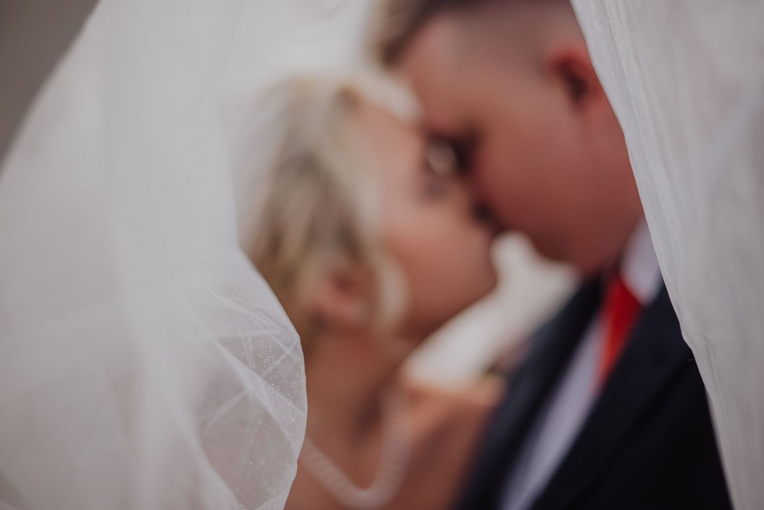 A romantic close-up shot of a wedding couple sharing an intimate moment through a delicate white veil.