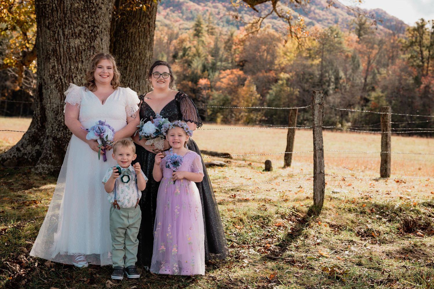 A family in coordinated white and pastel outfits poses together during a golden autumn sunset in a wooded setting.
