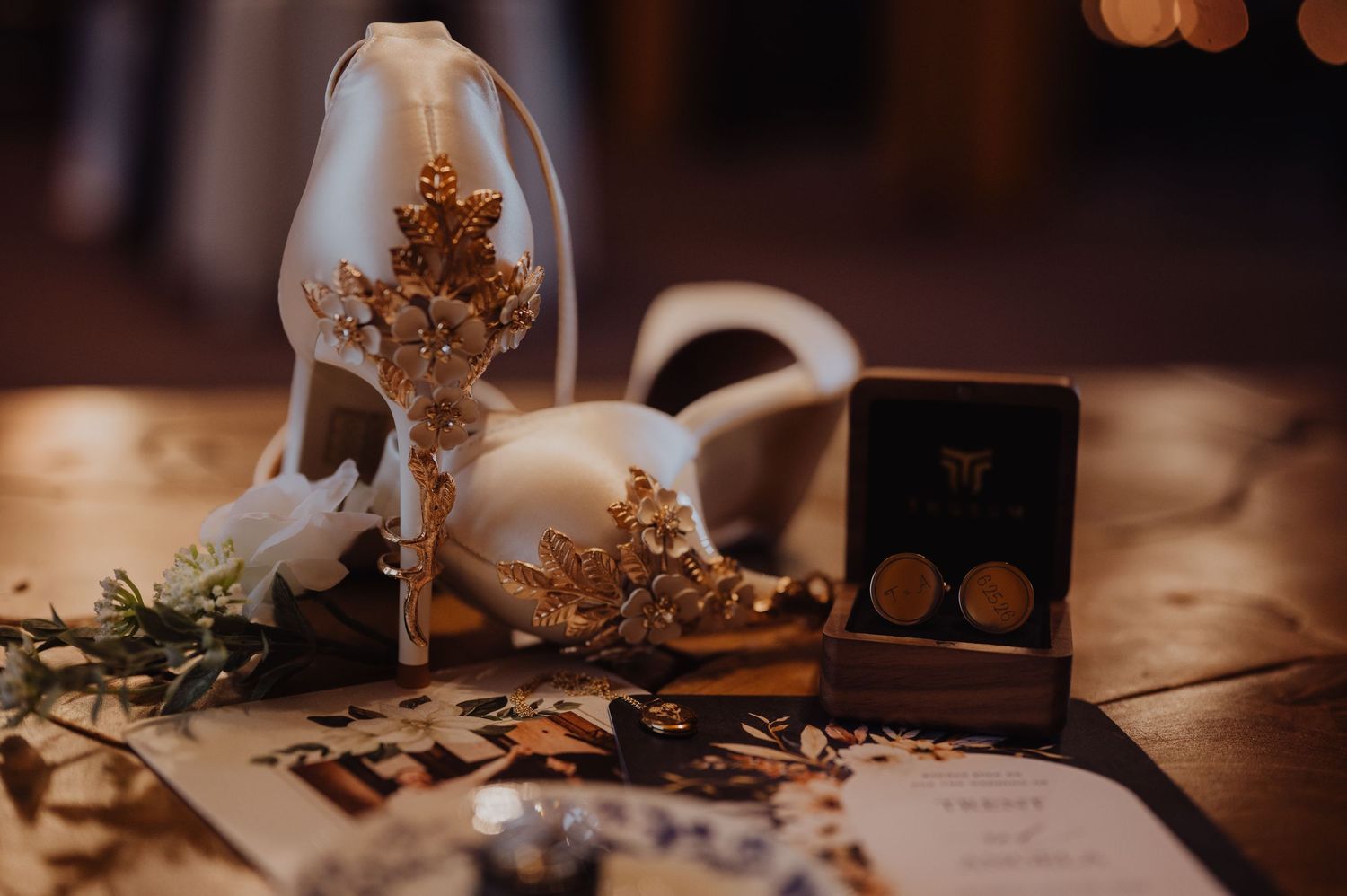 Elegant bridal accessories including white heels with gold floral details, pearl earrings in a box, and scattered gold confetti.