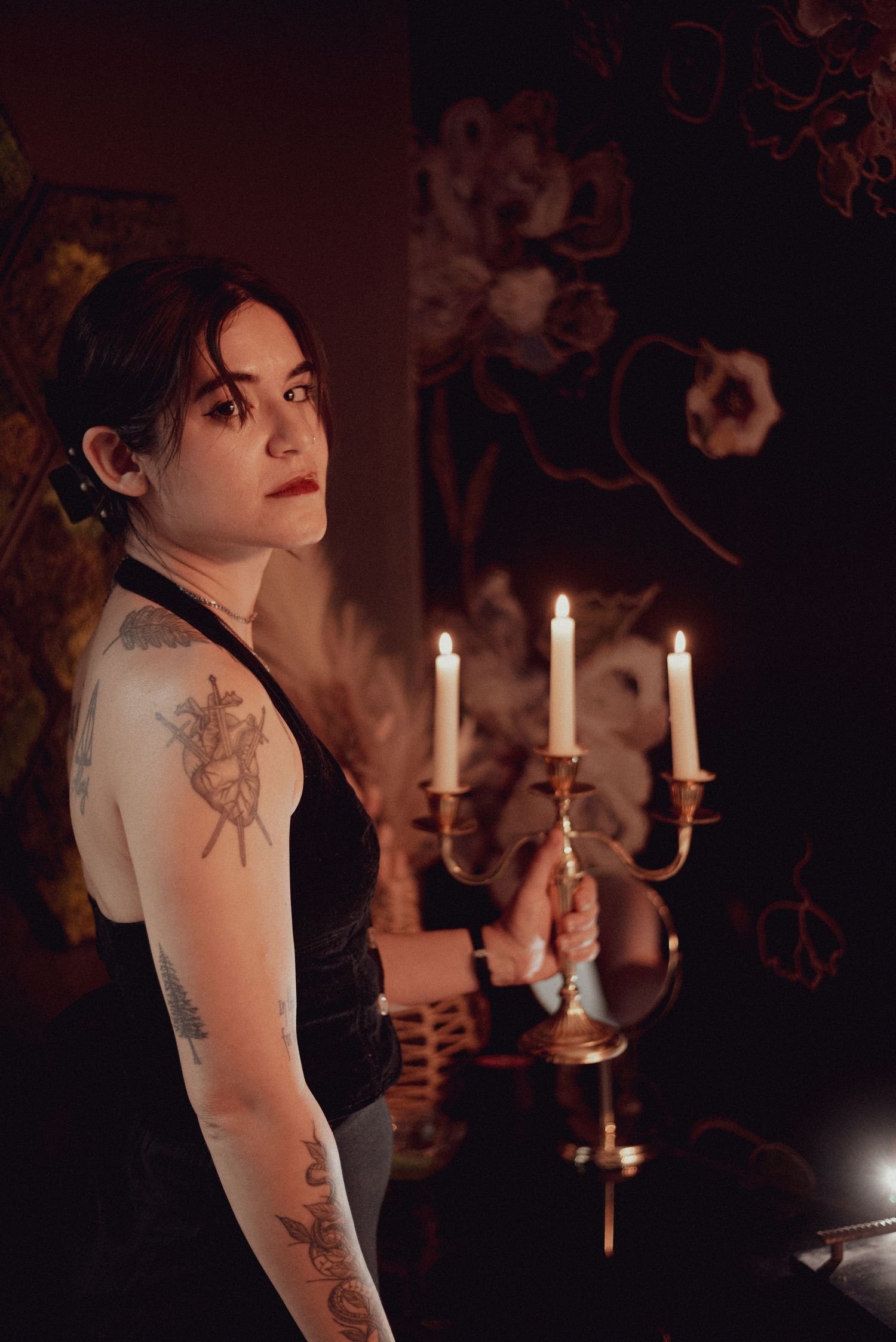 A moody portrait with candles featuring someone in black with visible tattoos.