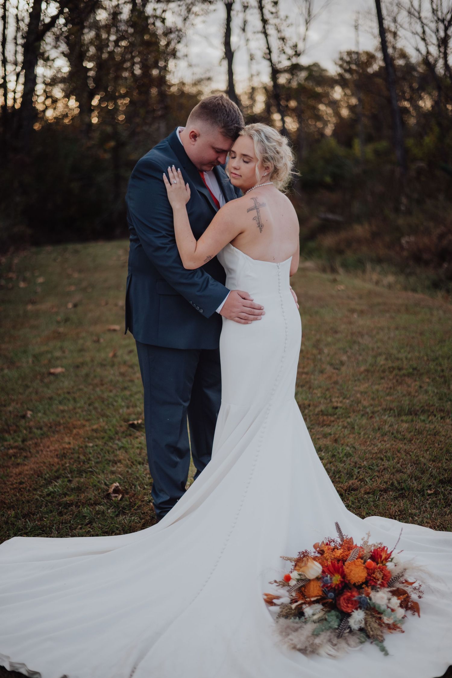 A tender wedding moment captured at sunset with a beautiful orange and white bouquet.