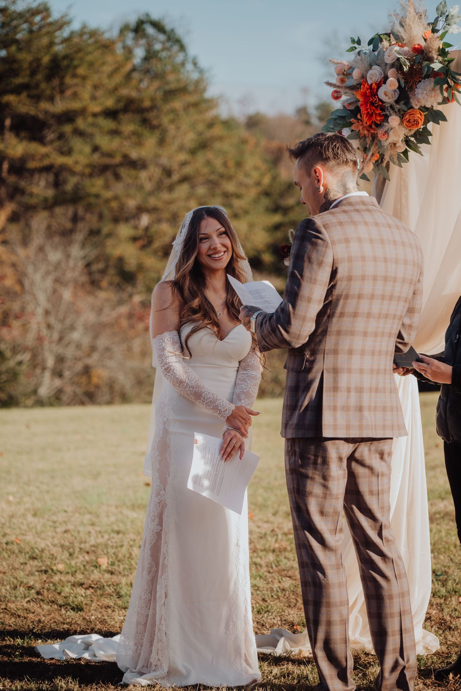 Wedding couple exchanging vows under a floral arch during an autumn outdoor ceremony.