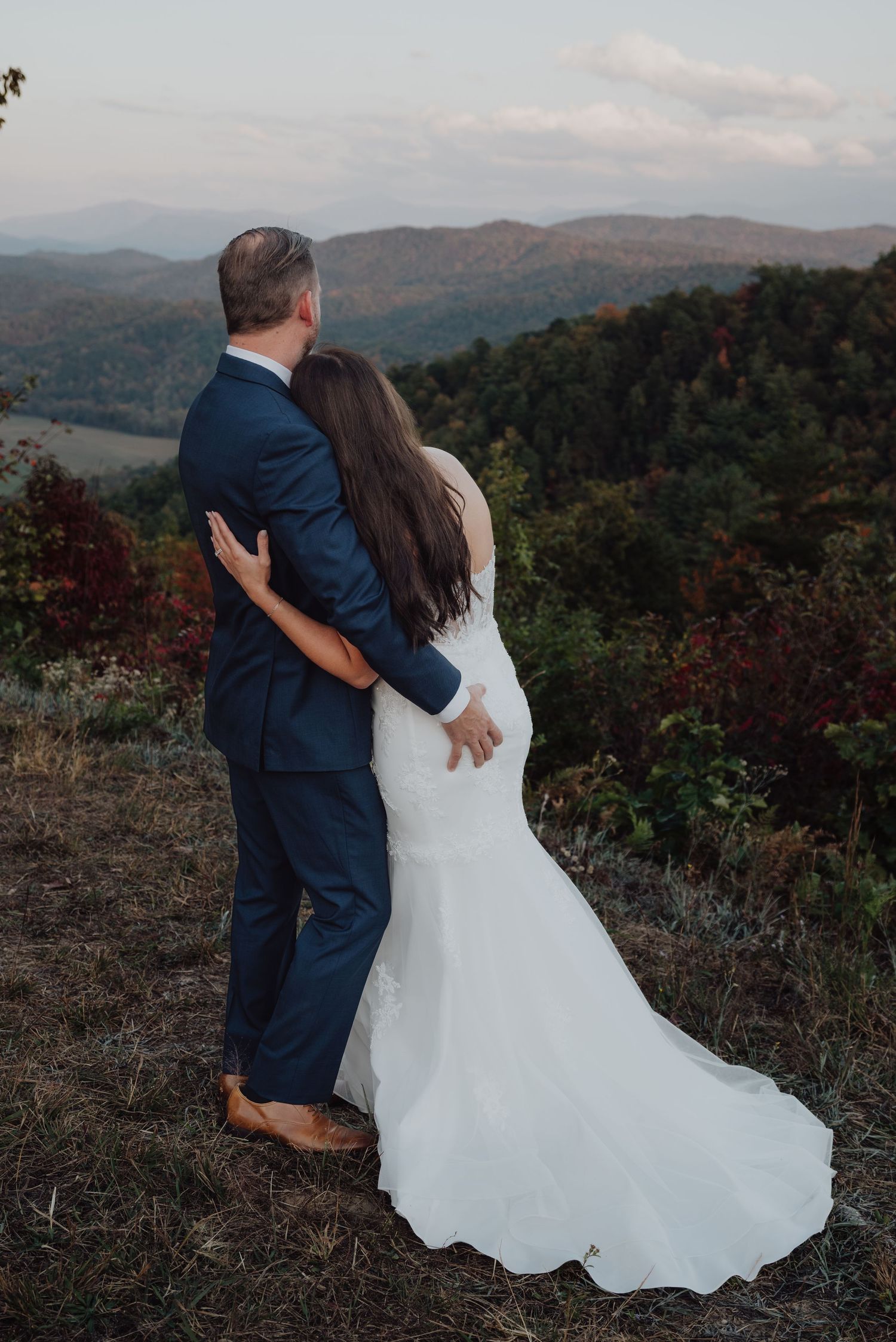 A couple embraces while overlooking a stunning mountain landscape on their wedding day.
