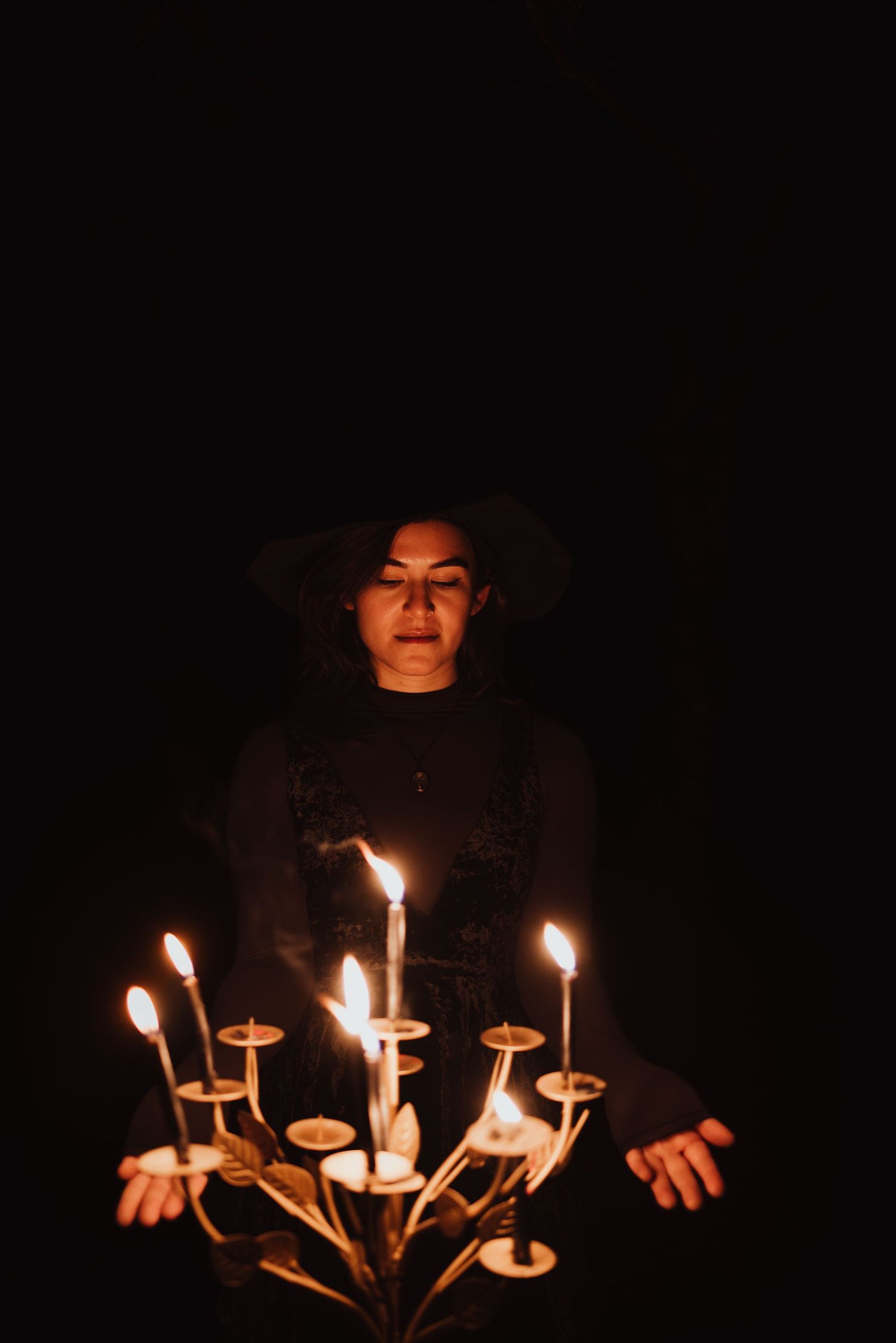 Dark moody portrait with candlelight from a branching candelabra creating dramatic shadows.