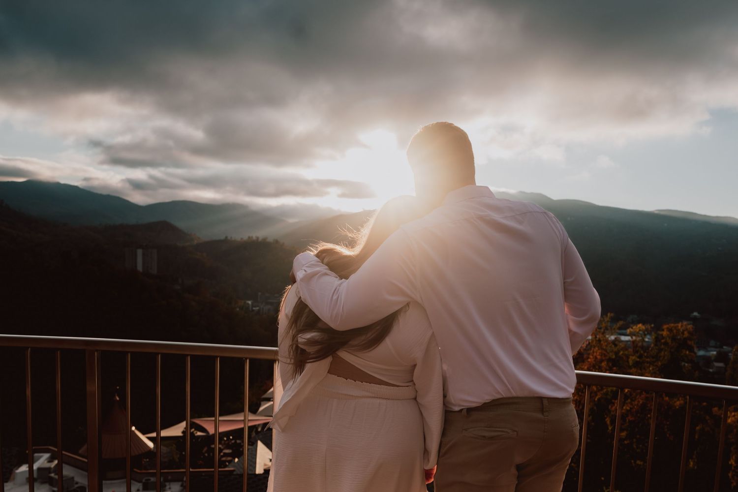 Dramatic mountain sunset silhouette of couple embracing on outdoor deck.