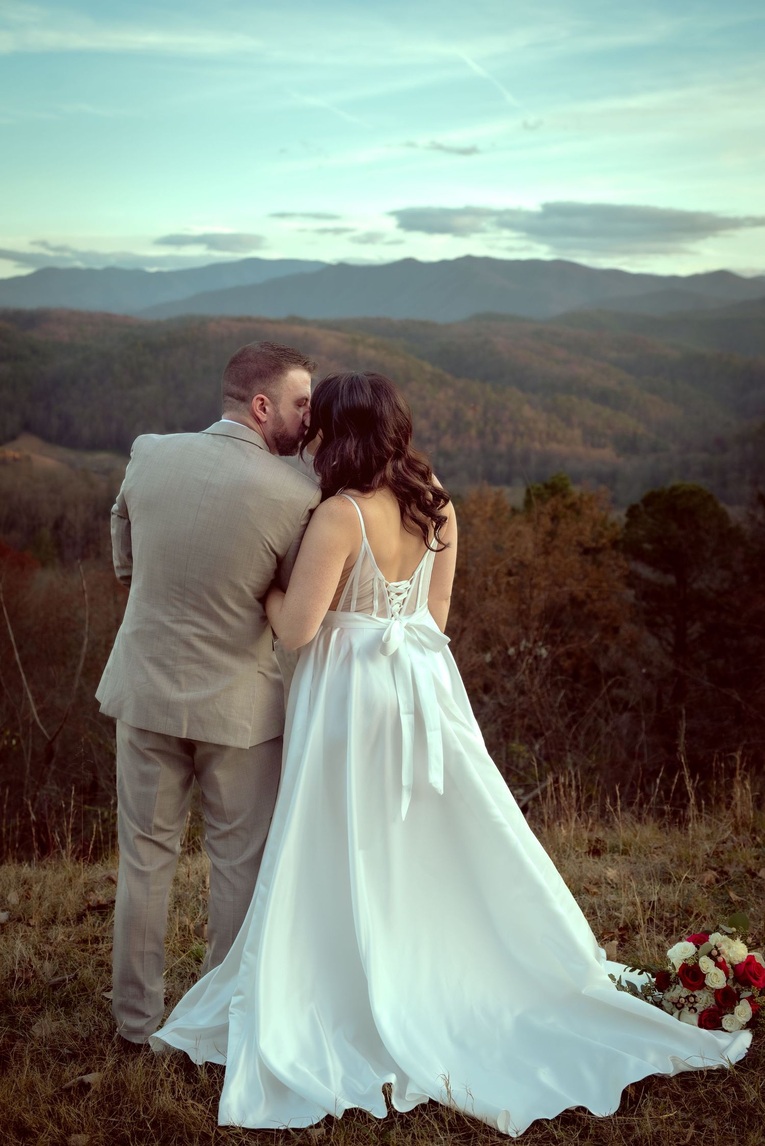 Elegant wedding couple embracing with mountain landscape in background.