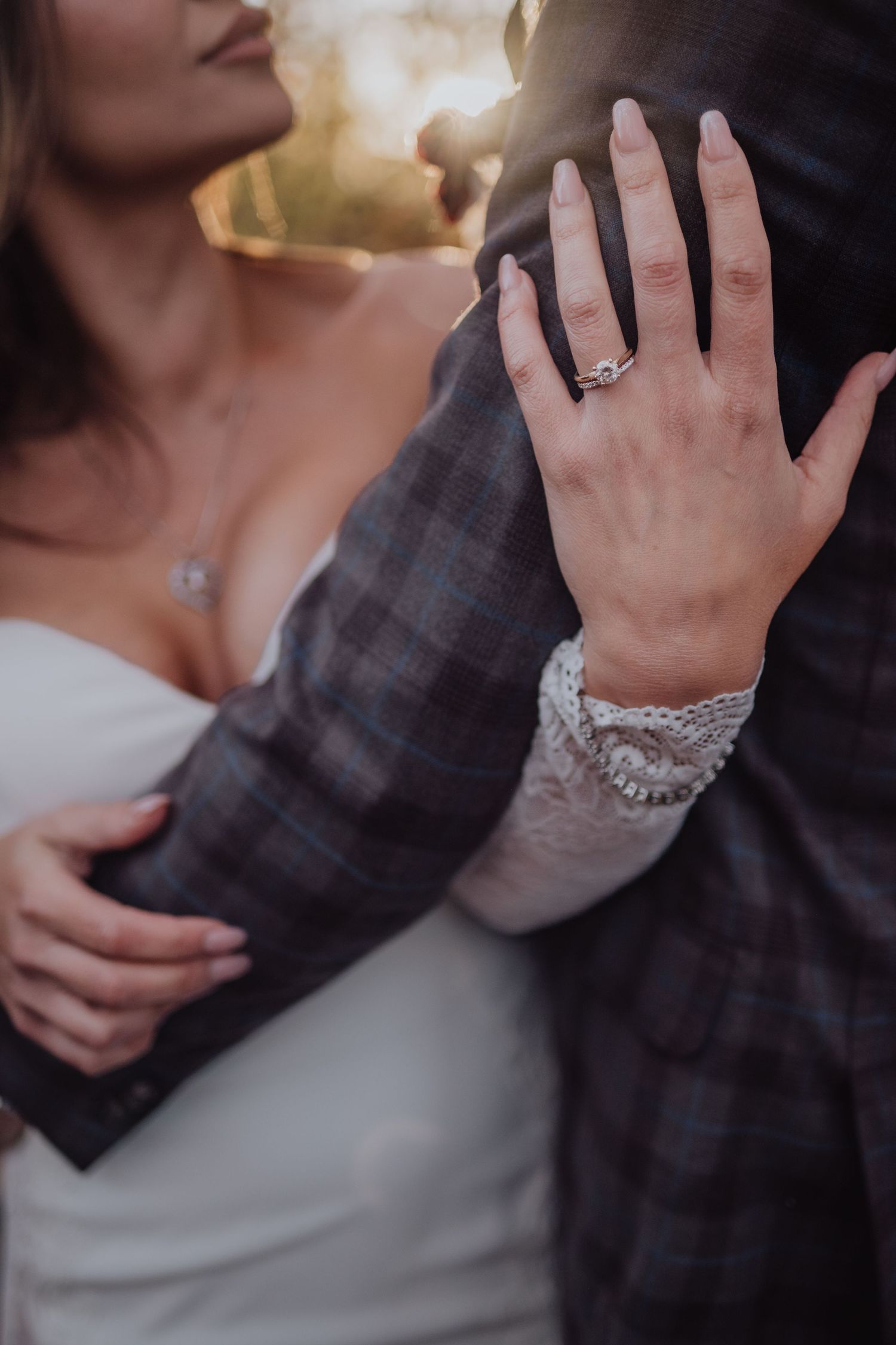 Close-up details of lace sleeves and engagement ring in warm golden light.