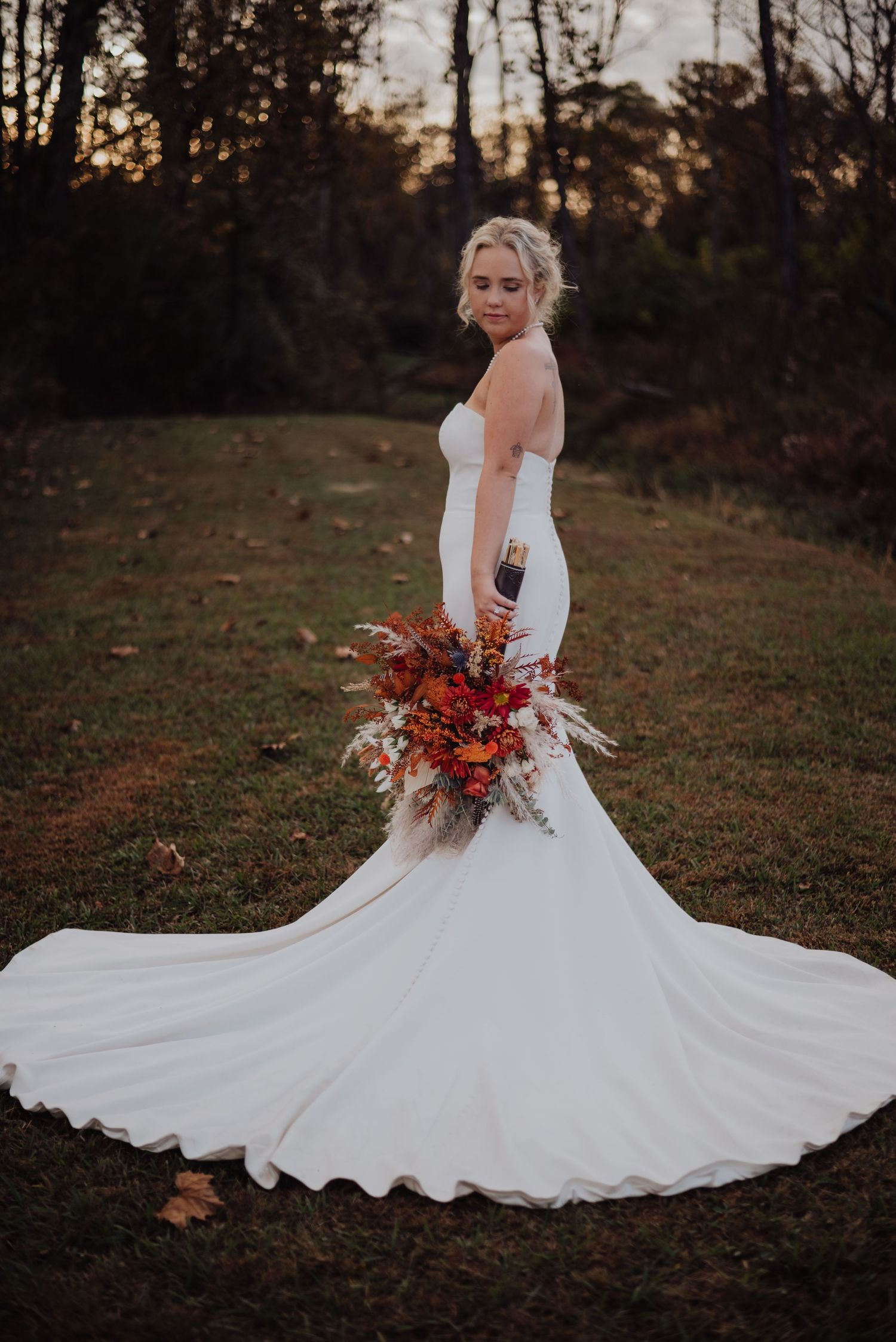 A bride in a flowing white gown twirls with her autumn bouquet at sunset.