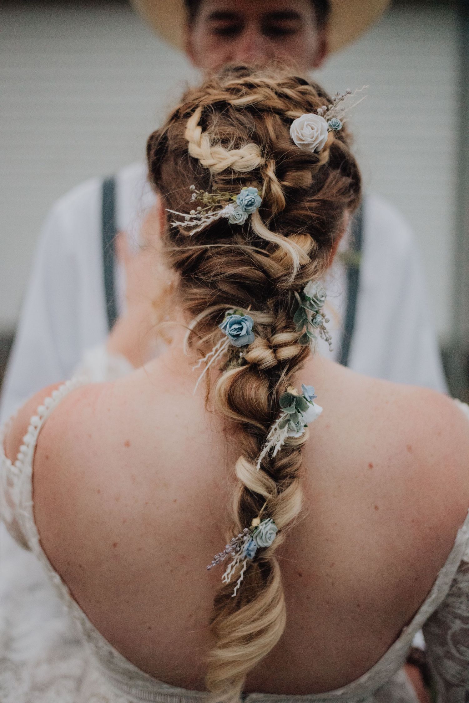 Intricate bridal hairstyle with delicate blue flowers woven through blonde braids.