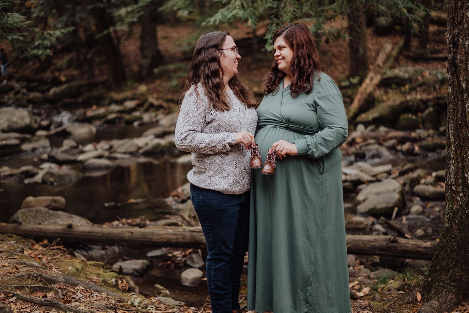 Two people share a joyful moment by a rocky stream in a forest setting.