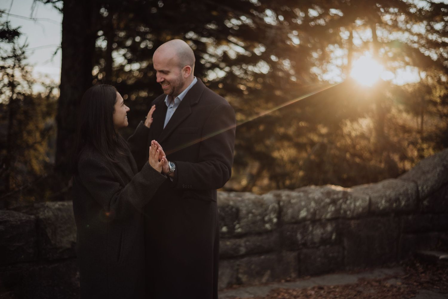 Couple sharing an intimate moment at sunset near a stone wall.