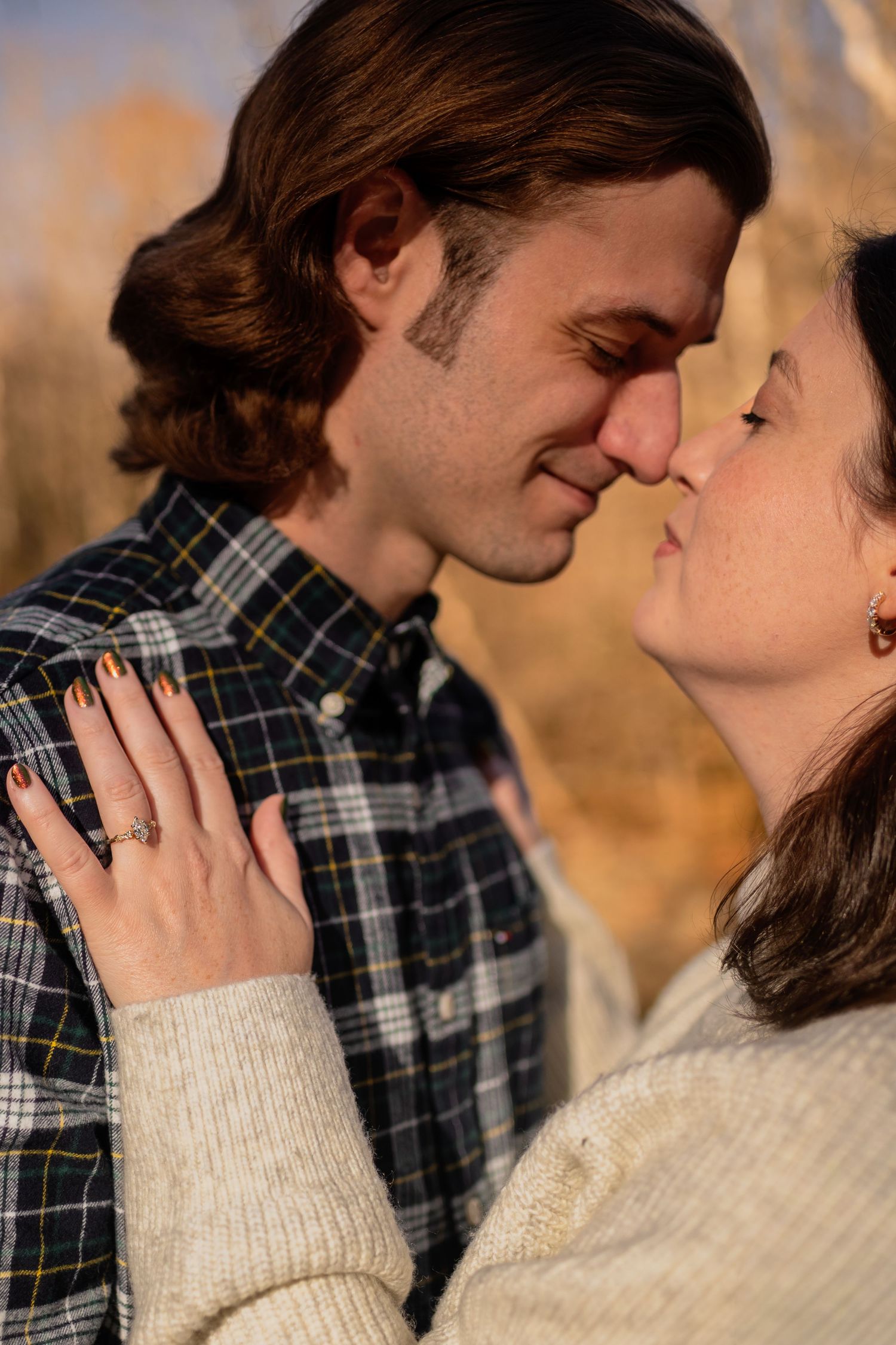 Intimate close-up portrait of couple in plaid and cream sweater during golden hour.