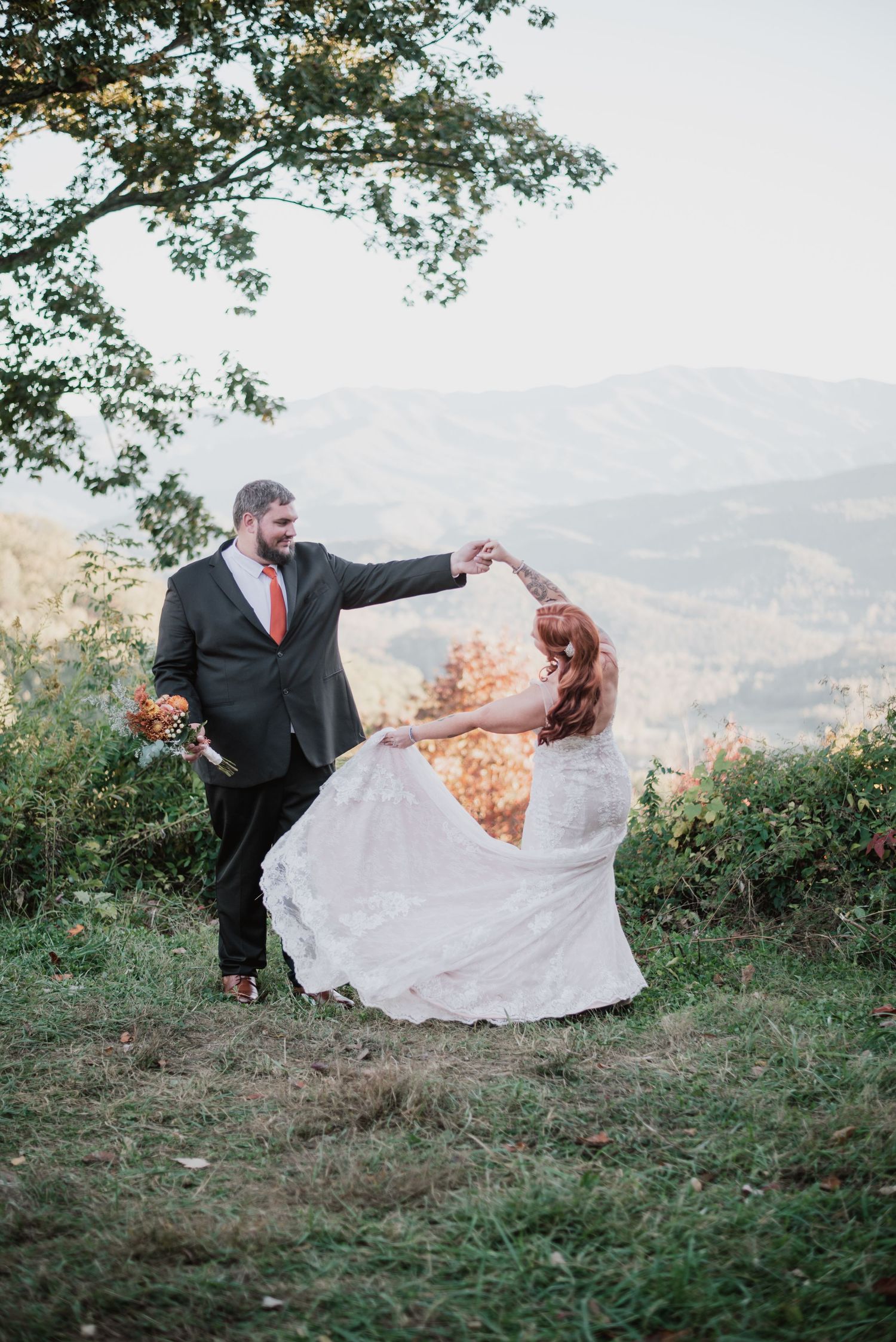 A romantic wedding couple dancing on a mountaintop with fall foliage in the background.