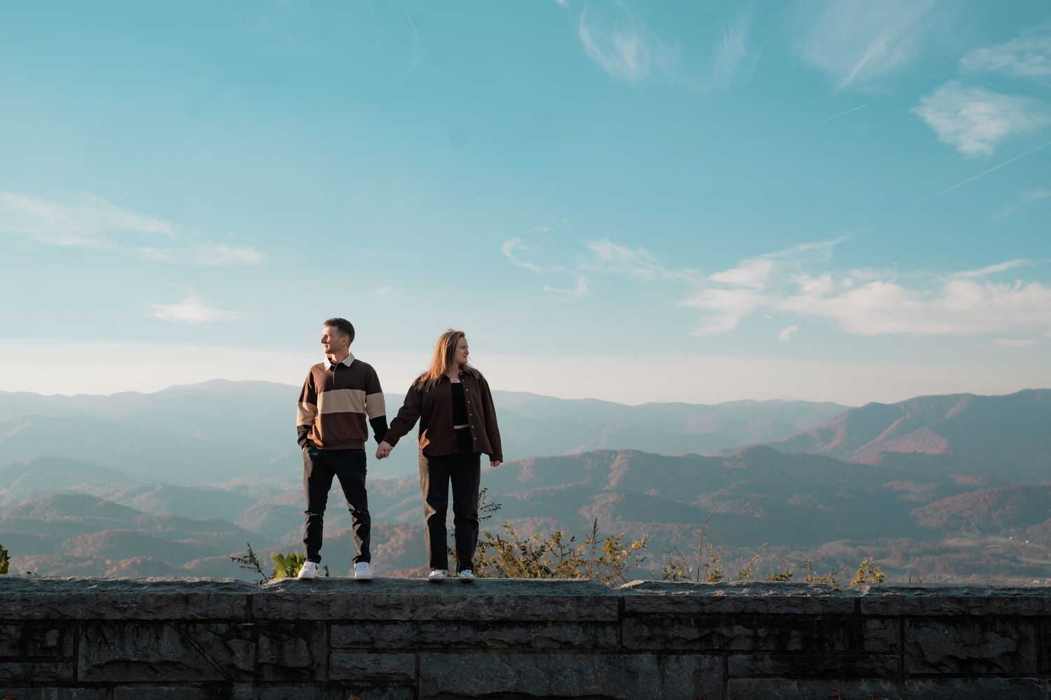 Silhouettes of a couple against mountain backdrop with blue sky and clouds.