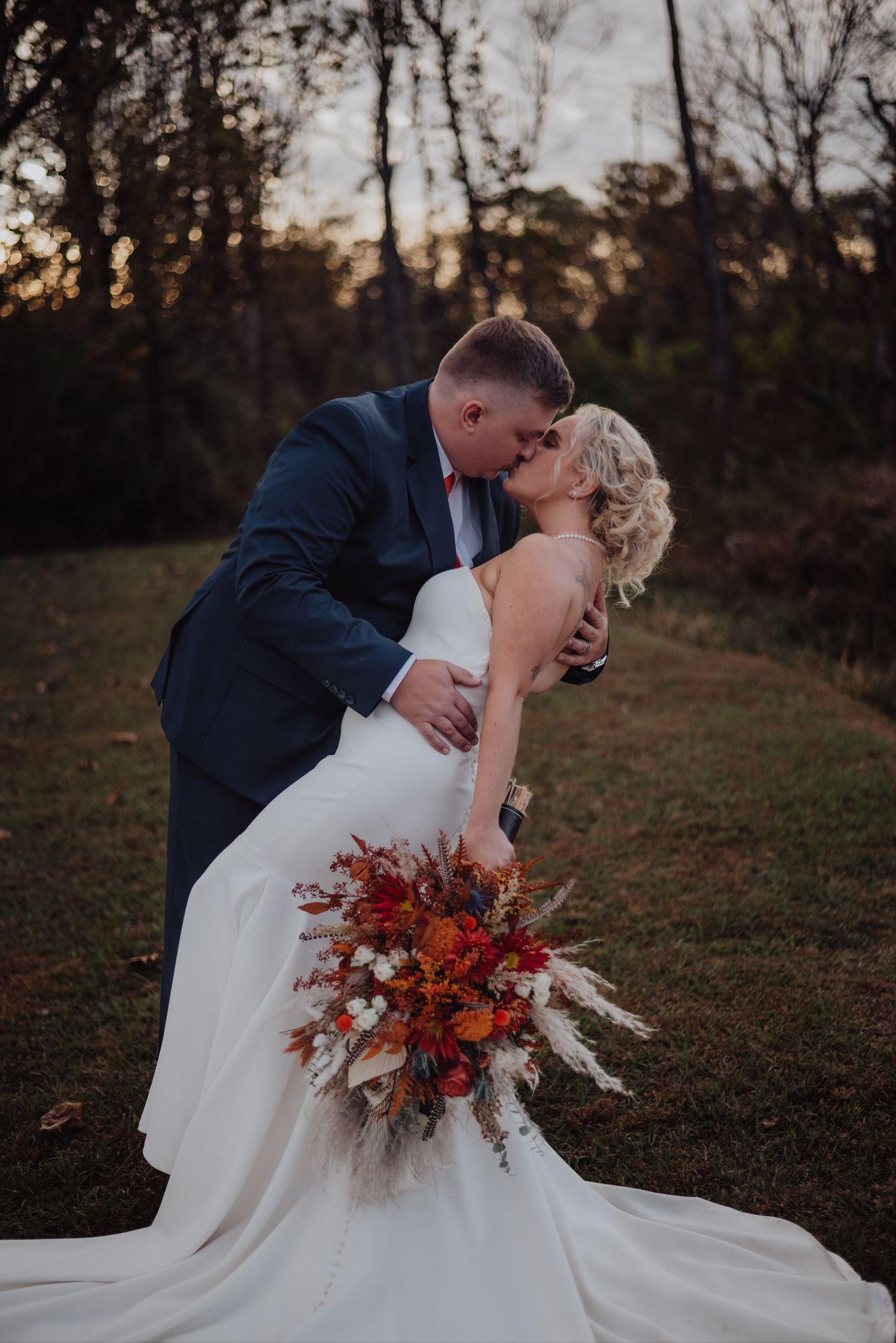 A romantic wedding dip pose with vibrant fall flowers against a sunset forest backdrop.