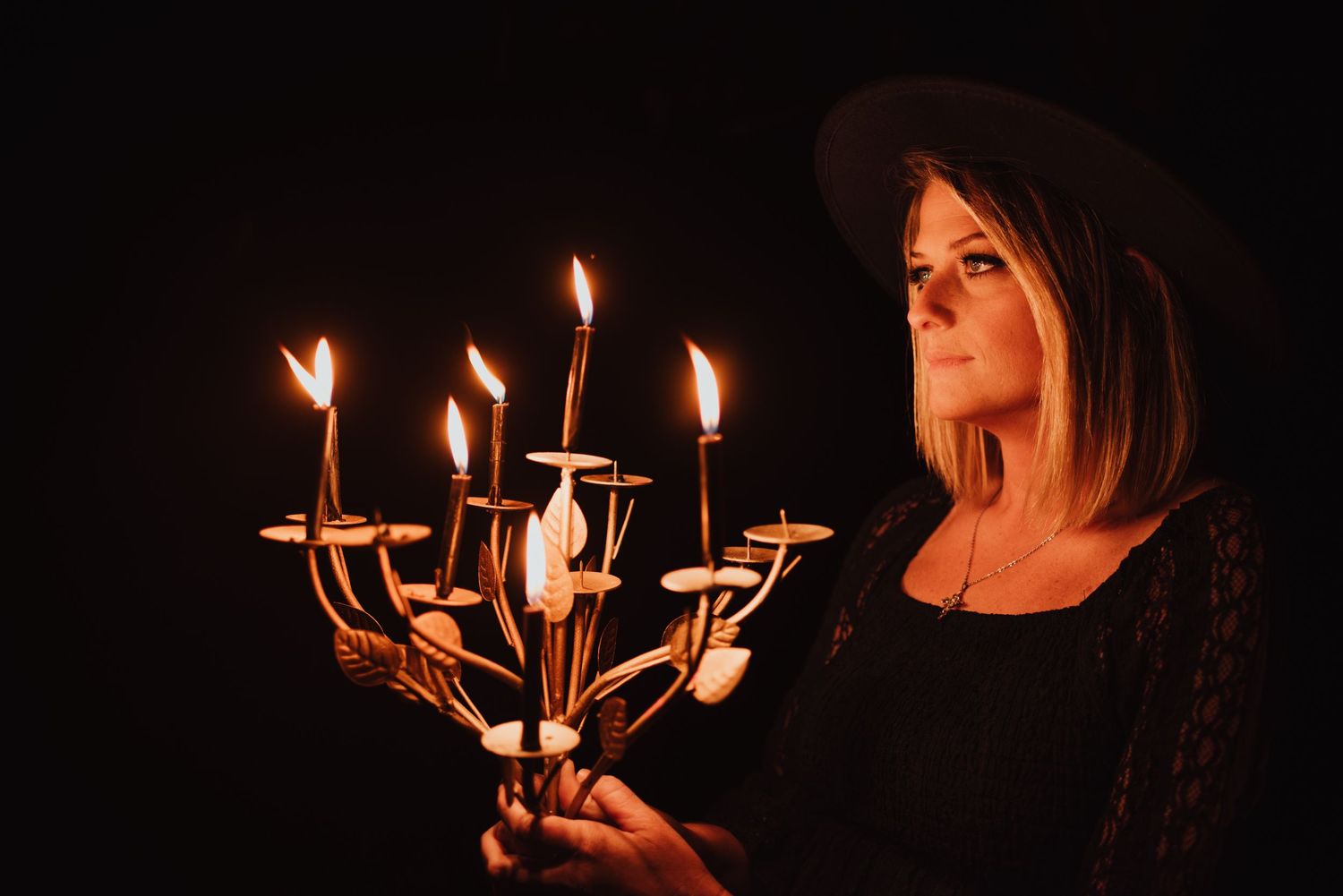 A moody portrait of someone holding a lit candelabra in darkness wearing black clothing.