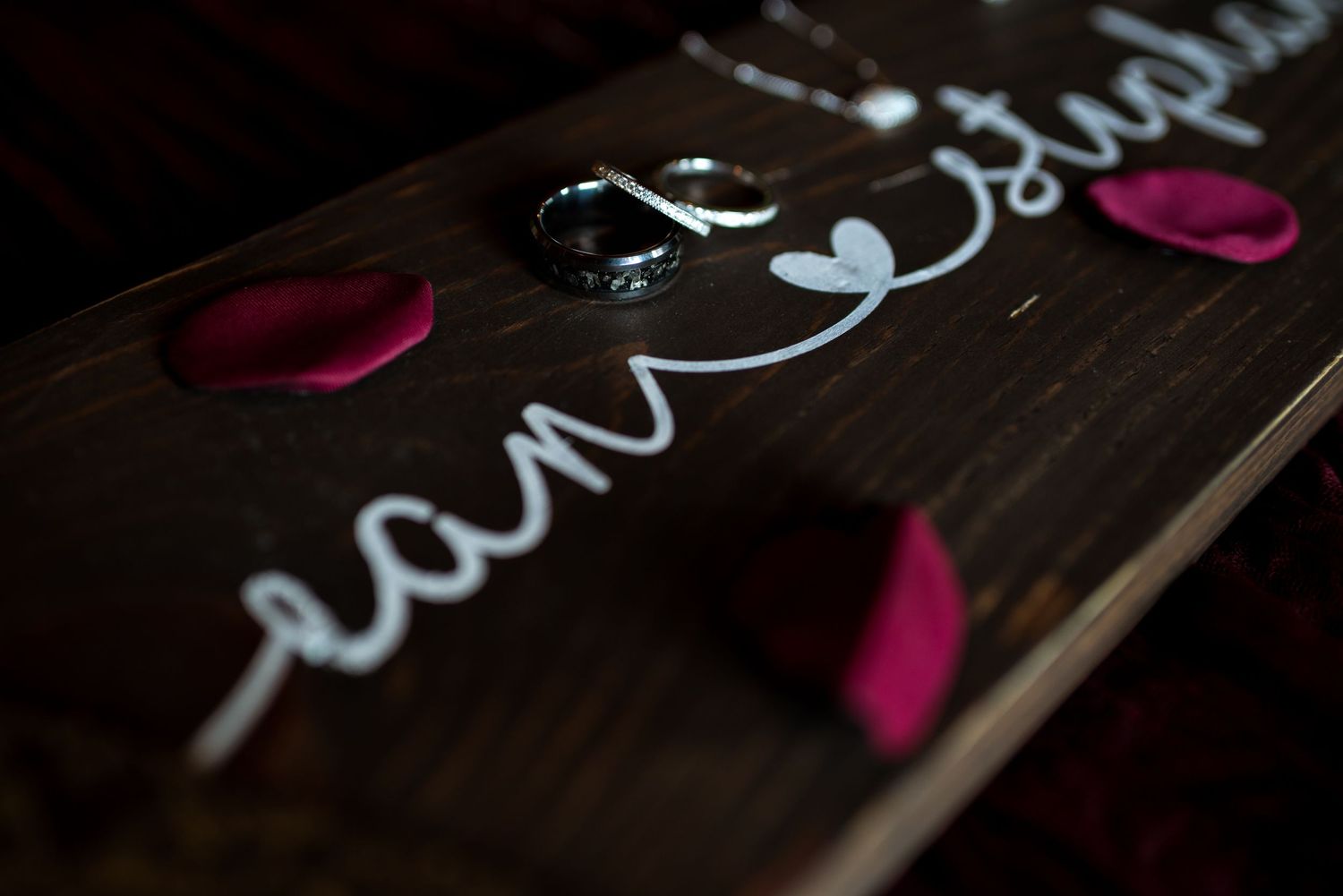 Artistic calligraphy writing in white ink on a dark wooden surface with pink accents.