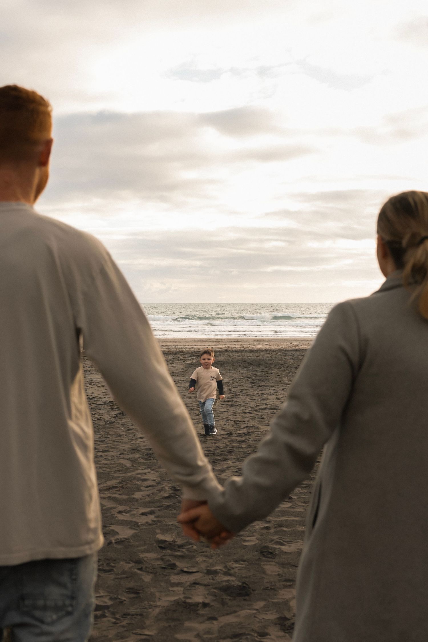 Family walking hand in hand along a misty beach shore during golden hour.