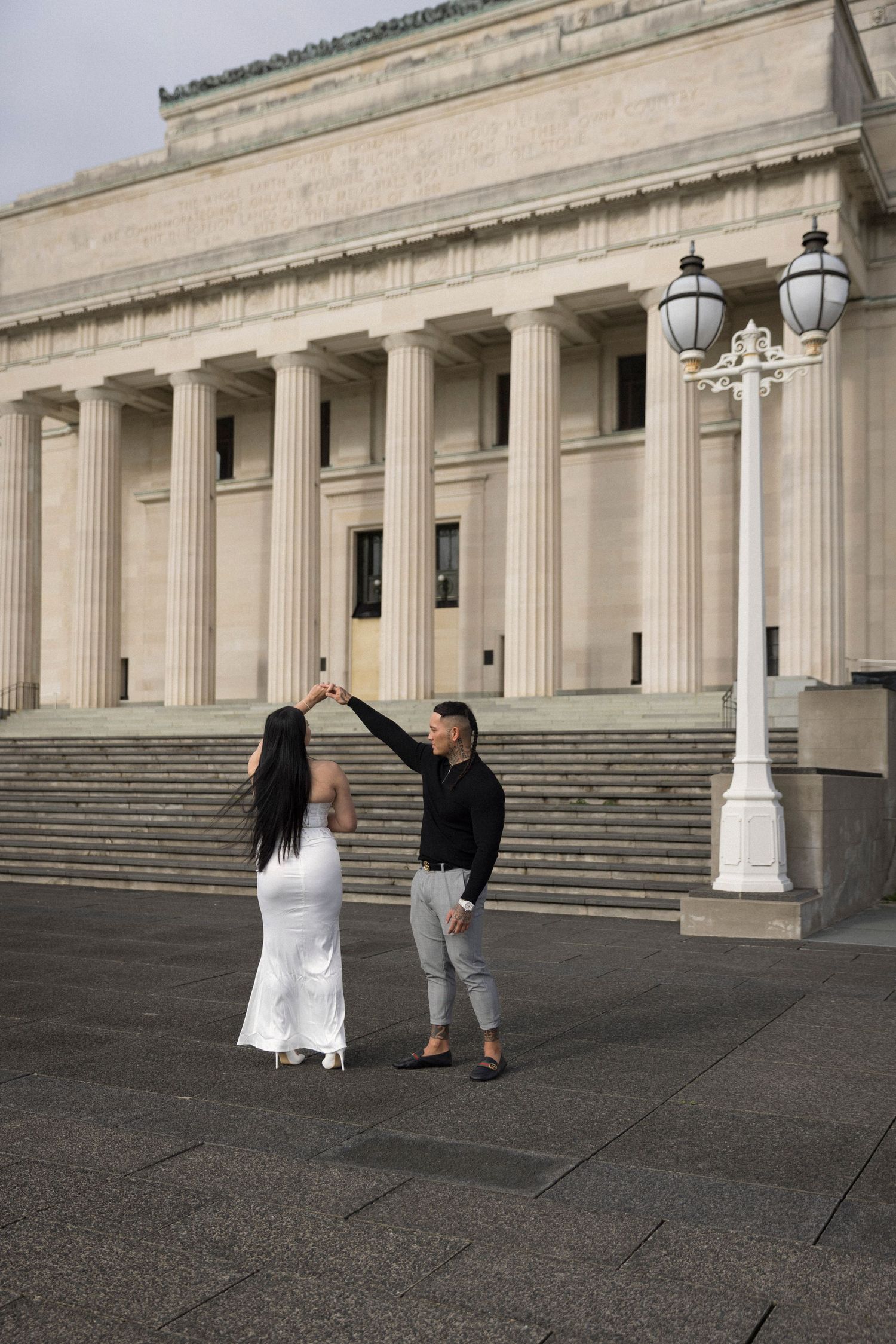 A couple poses for wedding photos in front of a grand neoclassical building with white columns and stone steps.