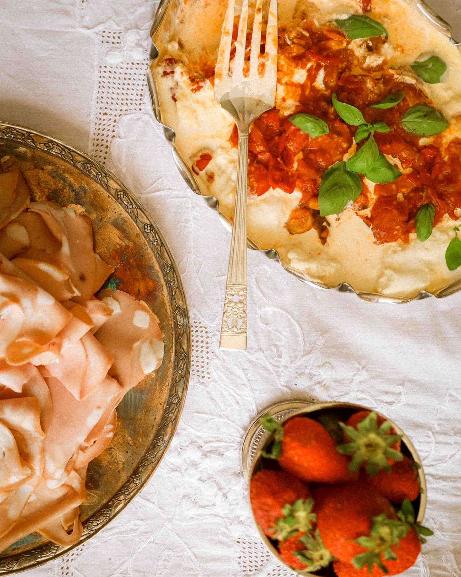 Elegant table setting with mashed potatoes topped with tomato sauce and basil, sliced turkey, and fresh strawberries.
