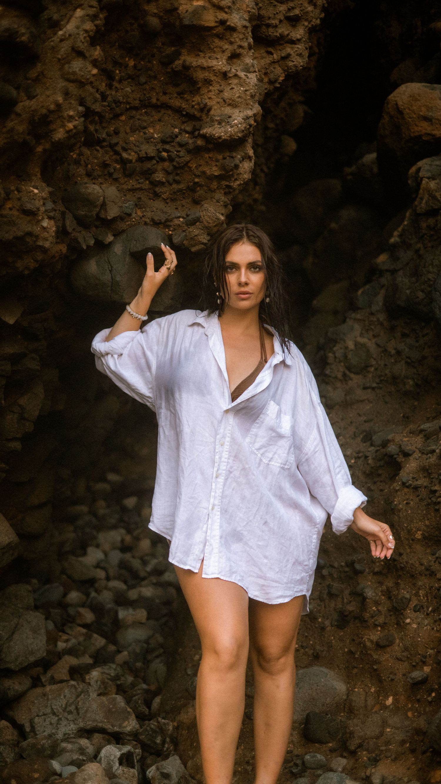 Figure strikes dynamic poses in white shirt against textured cave backdrop.