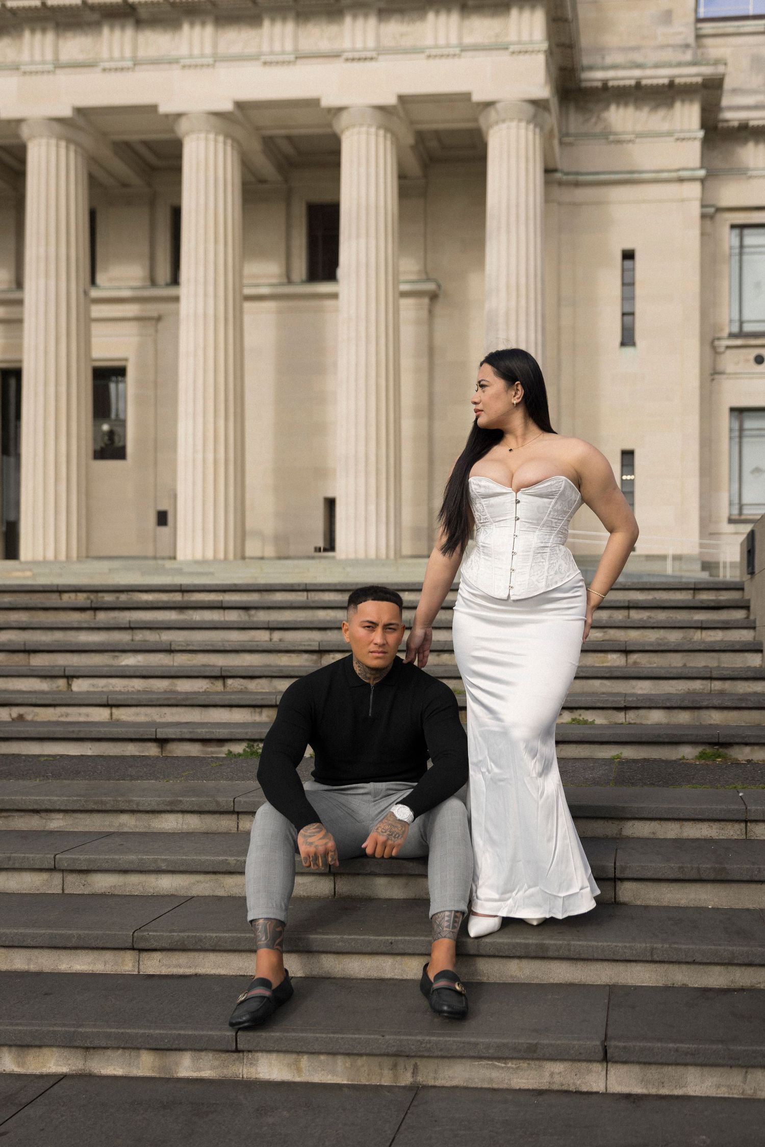 Couple in formal attire posing on grand stone steps of a classical building.