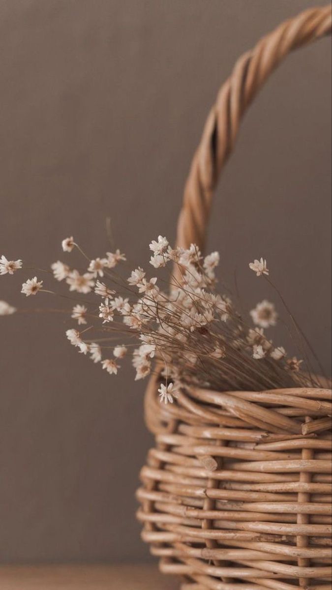 Delicate white dried flowers arranged in a rustic woven wicker basket against a neutral brown background.