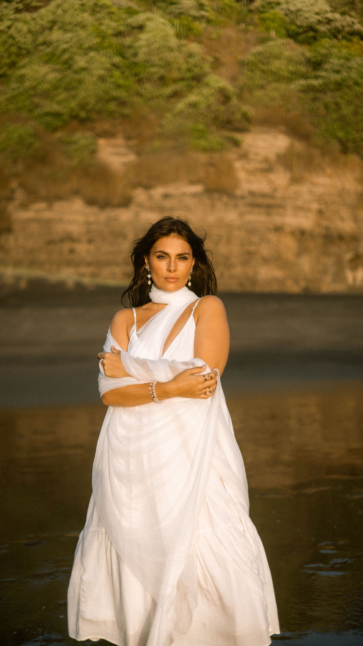 A white dress billows in the wind against rugged coastal cliffs and ocean waves.