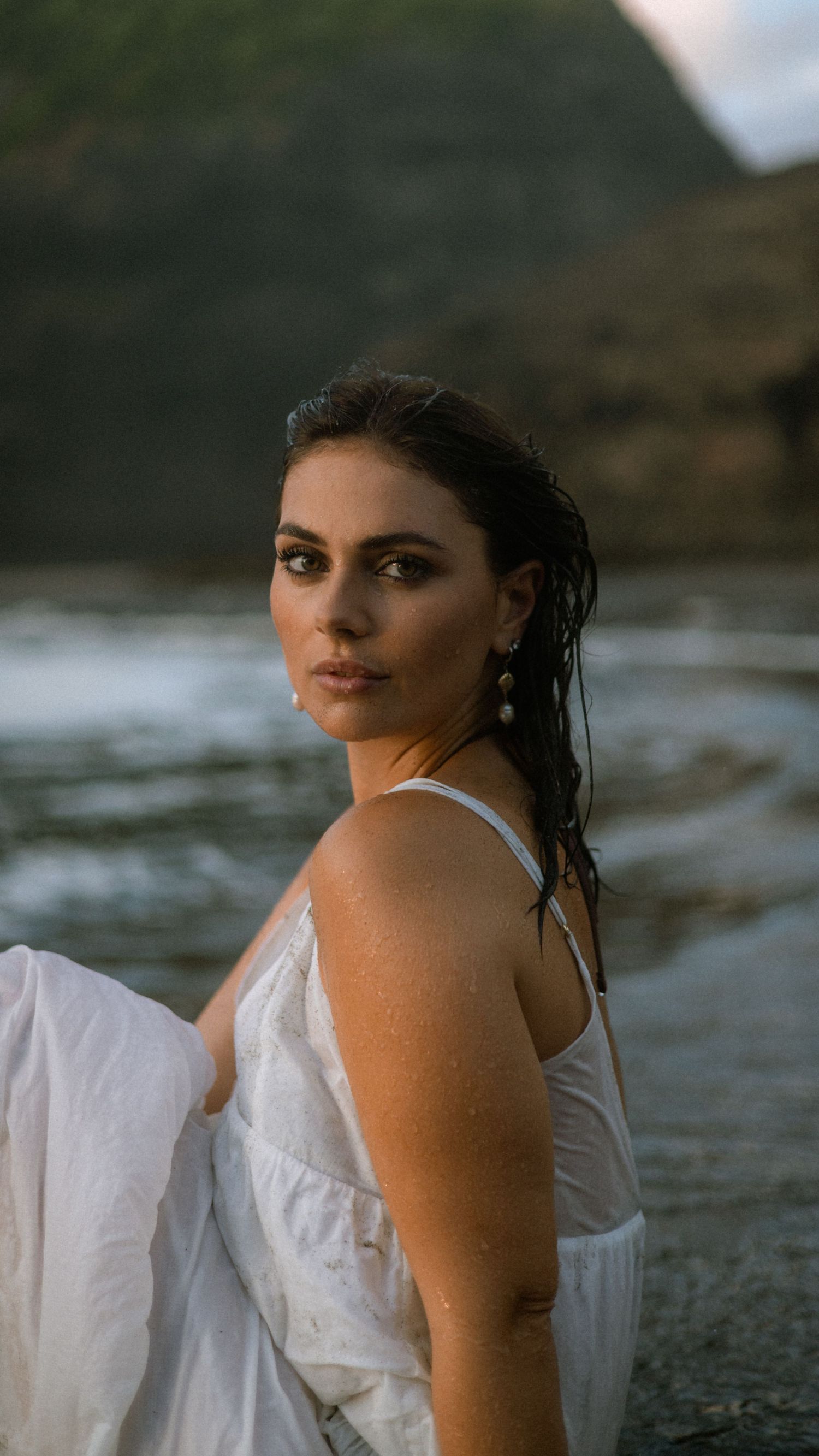 Artistic coastal photoshoot featuring white dress against dramatic ocean scenery.