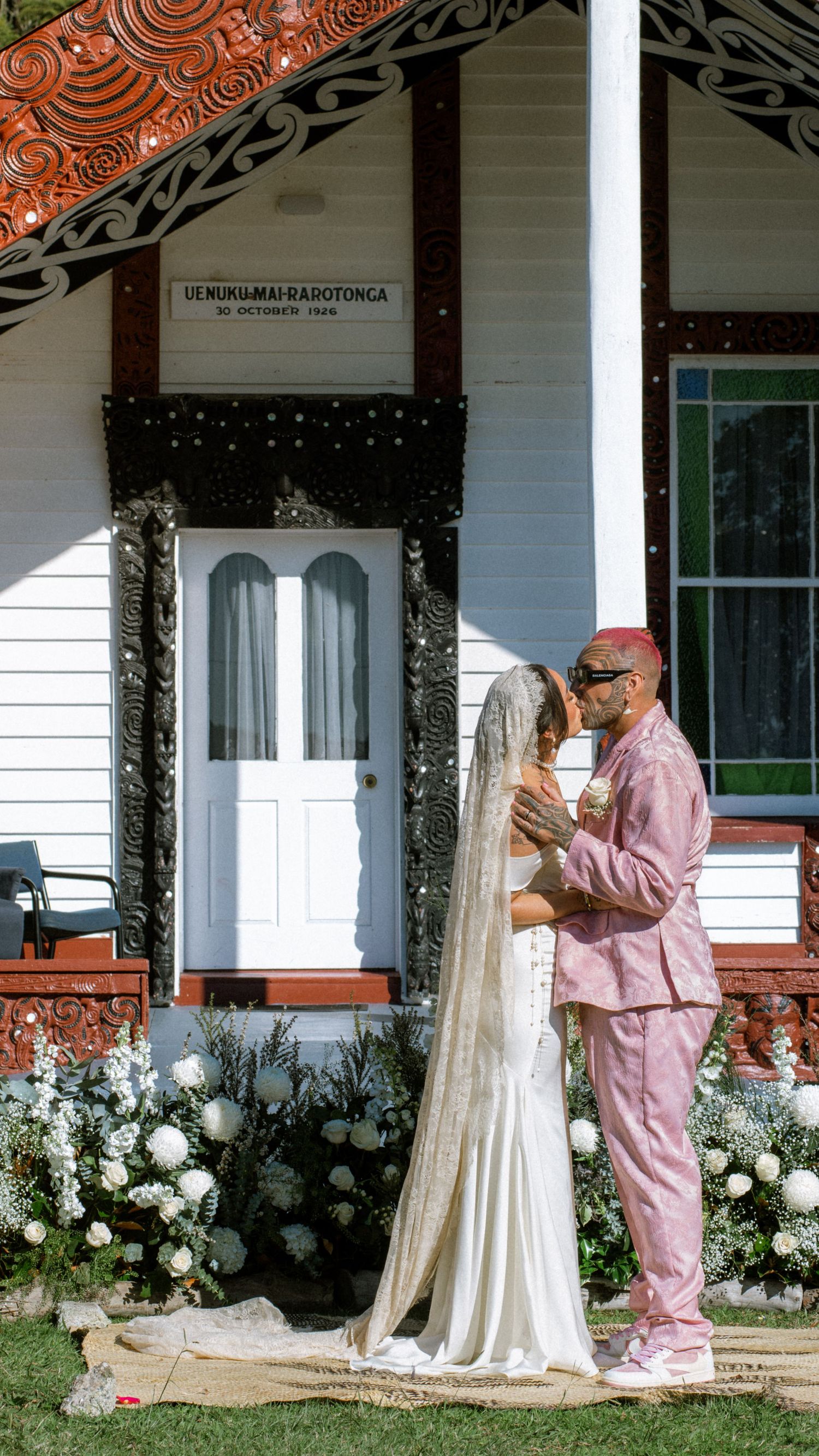 Four sequential photos show a traditional Maori meeting house with ornate carvings and white roses blooming along the veranda.