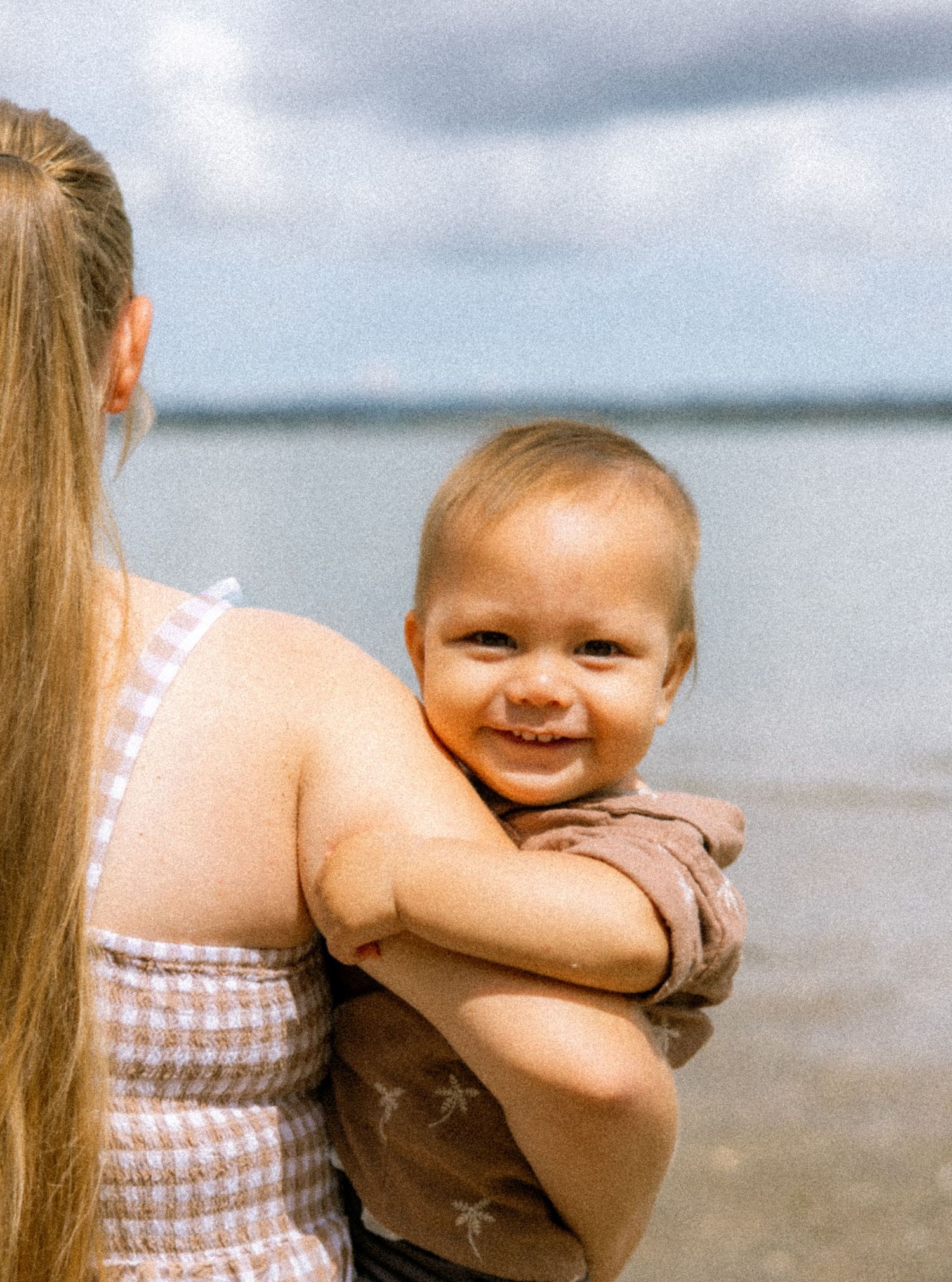 A series of four similar photos showing a baby in a brown outfit smiling at the beach with water in the background.