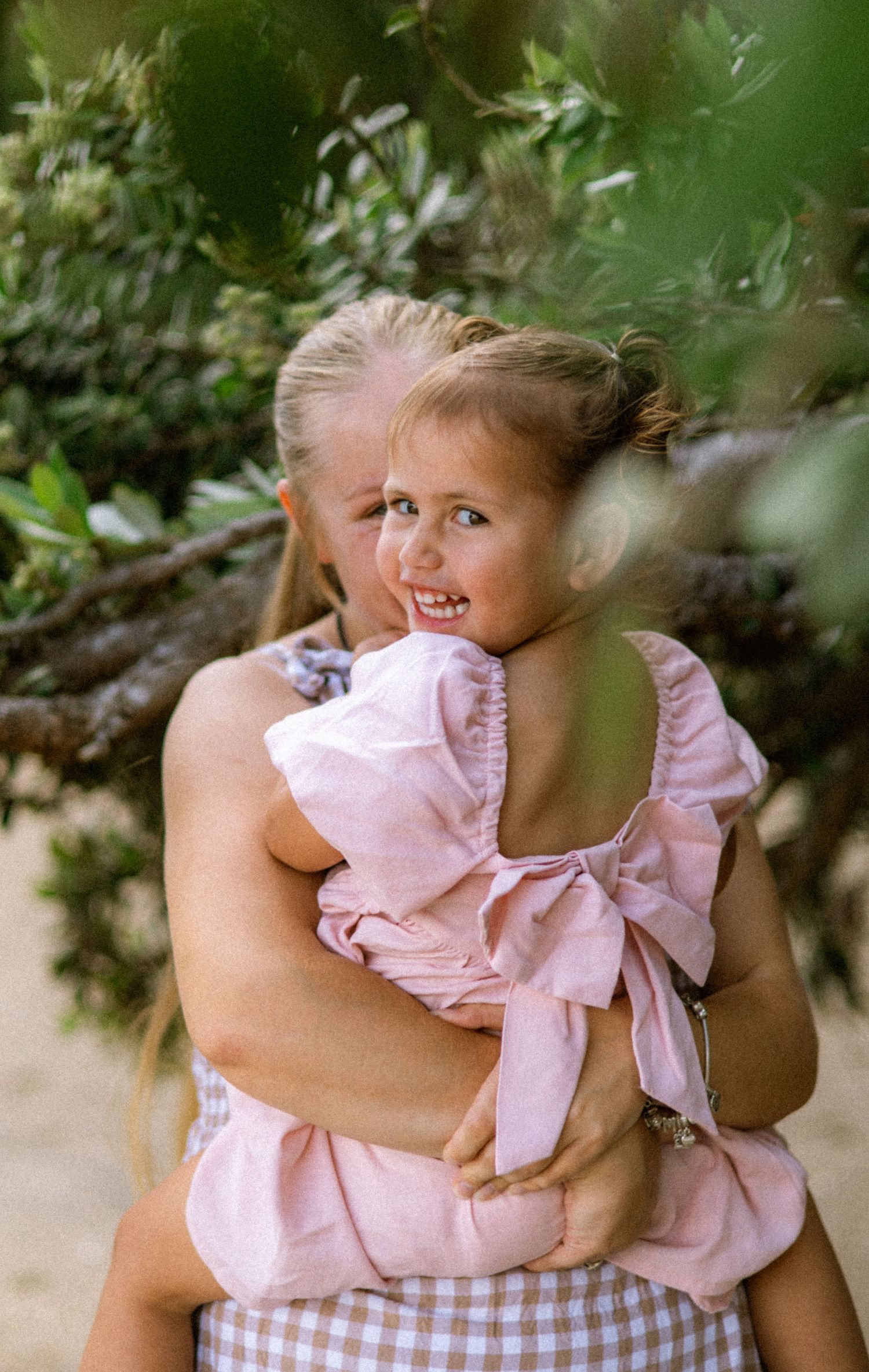A series of candid photos showing a child in a pink dress playing and being held outdoors among greenery.
