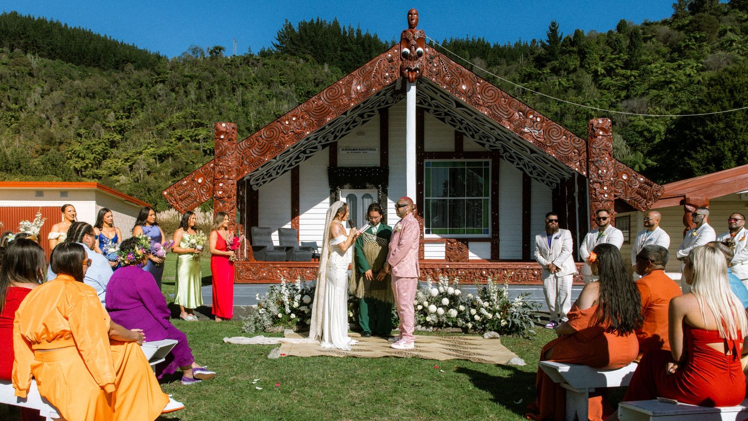 A panoramic view of a traditional Maori meeting house with carved wooden details and lush green surroundings in New Zealand.