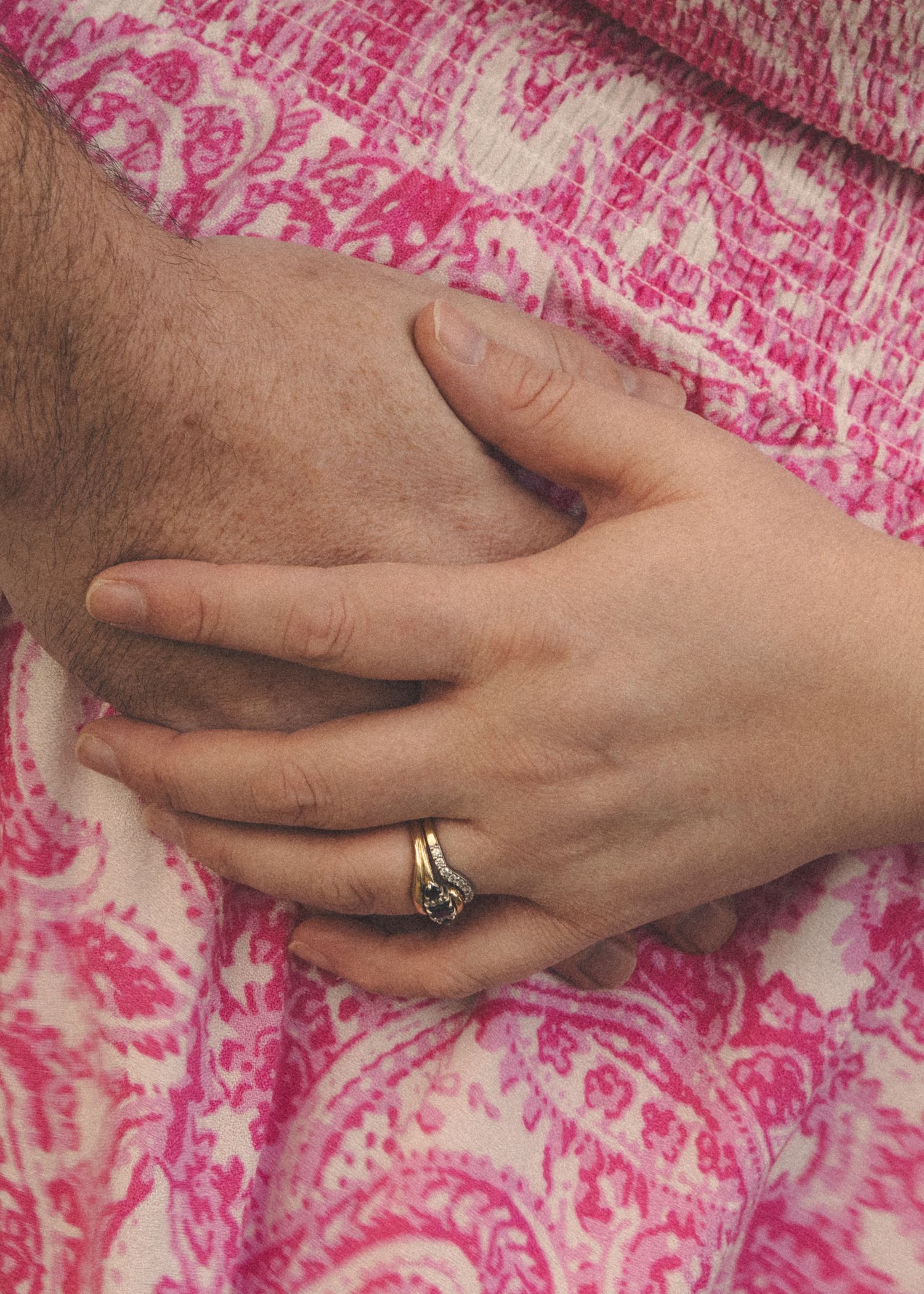 Close-up of hands with engagement ring resting on pink patterned fabric.