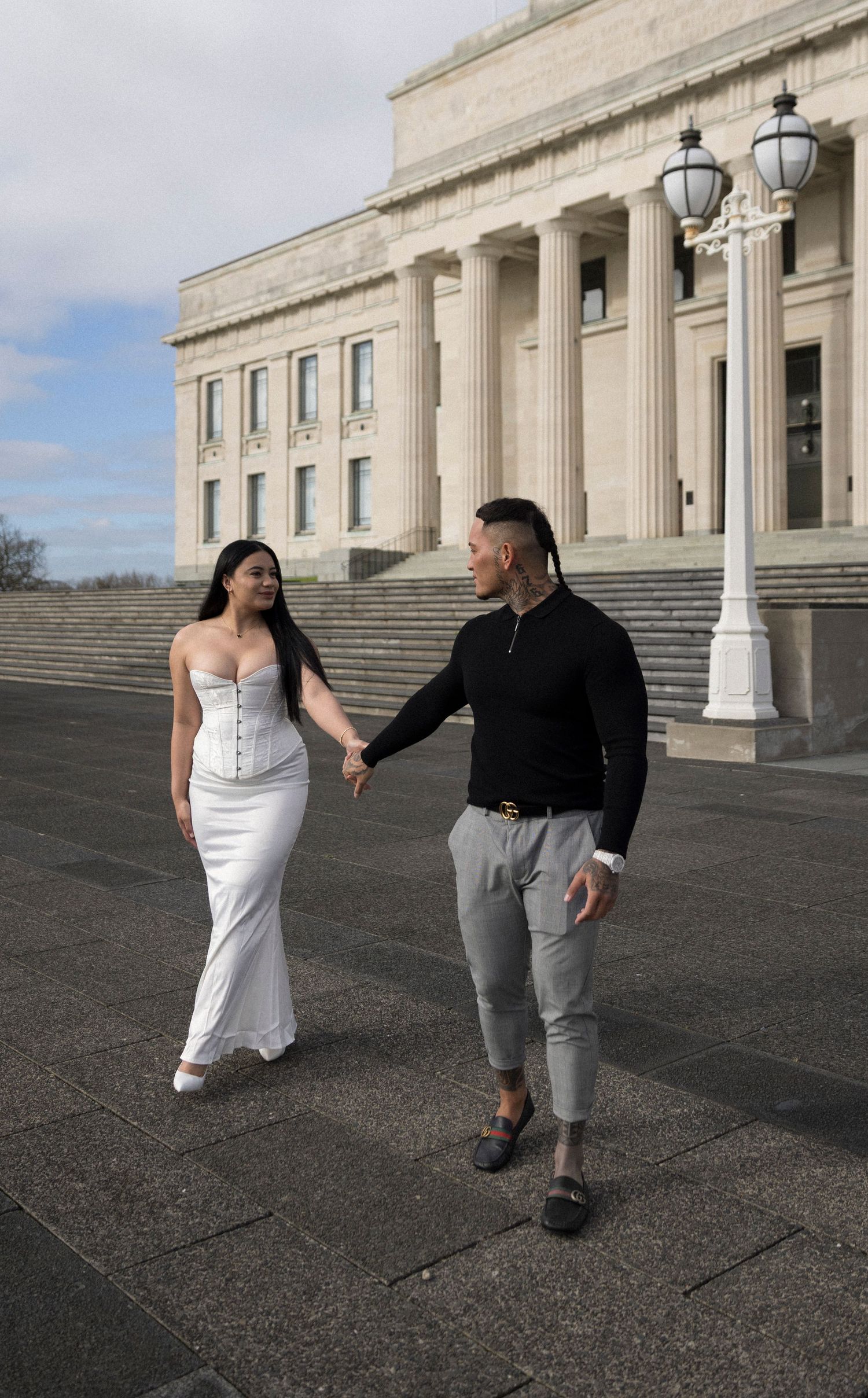 A couple in wedding attire poses playfully on the steps of a grand neoclassical building with white columns.