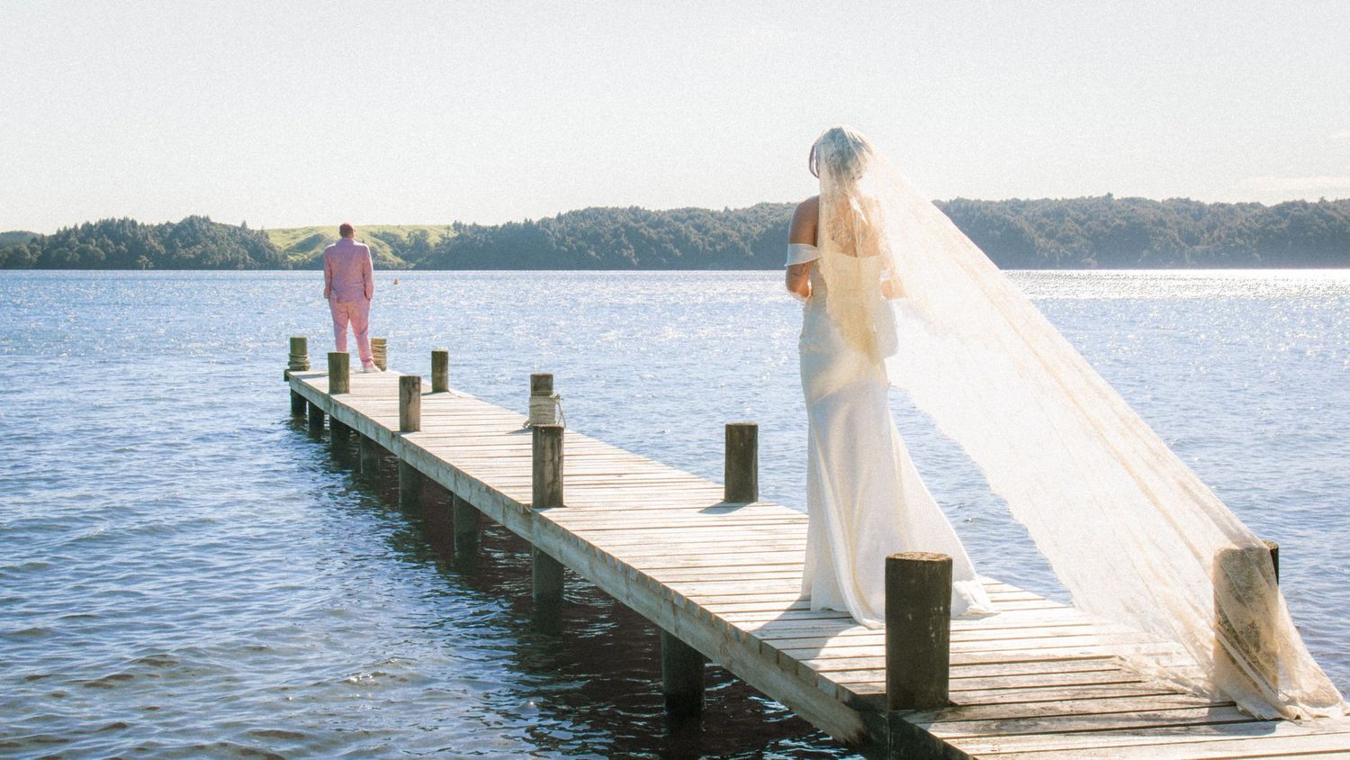A romantic scene unfolds on a wooden dock by the lake at sunset with flowing white fabric in the breeze.