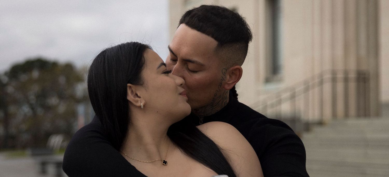 Intimate moment captured between couple against classical architecture background.