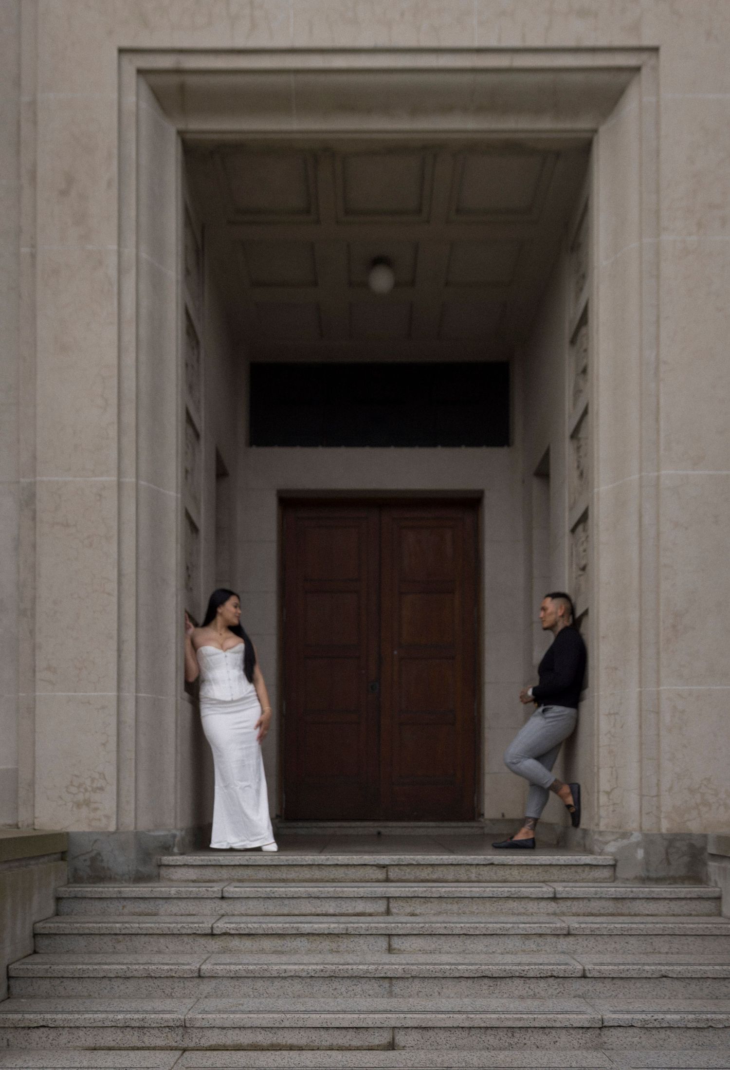 Two people standing in an elegant stone doorway with classical architecture and steps.