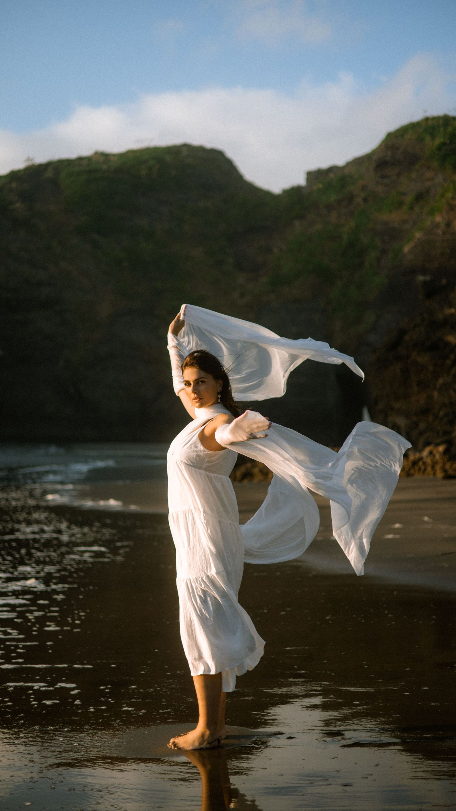 Graceful dance poses performed on a black sand beach with mountains and ocean waves.