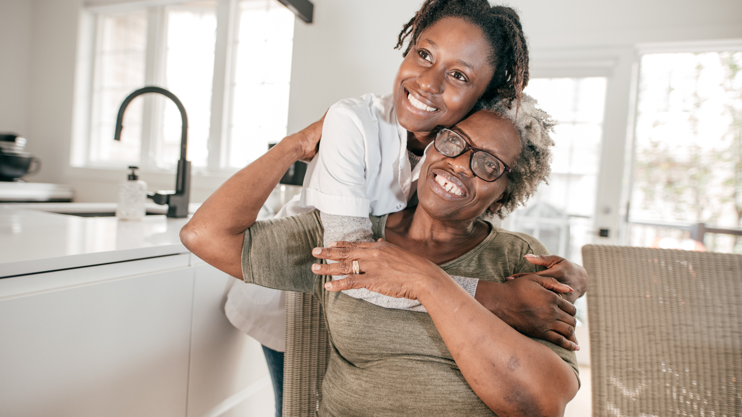 A daughter laughs and hugs their mother while relaxing on a couch in a bright, modern living room.