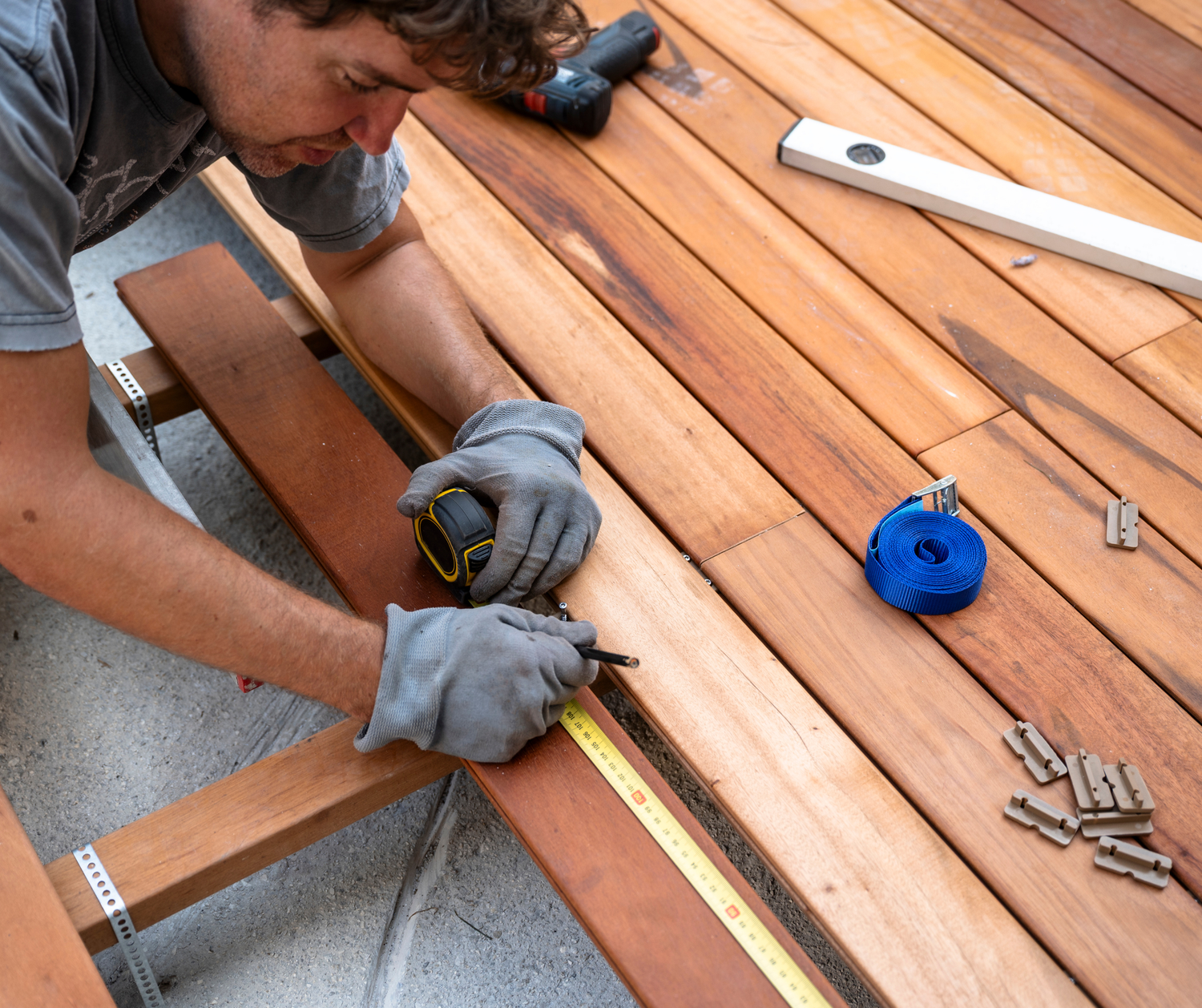 Person using power tools and measuring tape to install deck boards during outdoor home improvement project.
