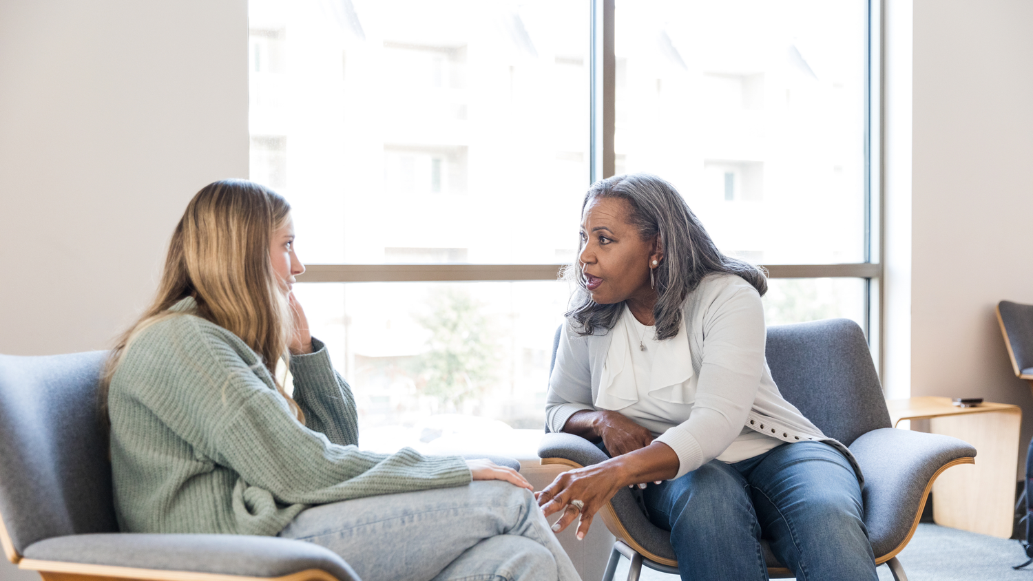 People sit in a therapy or counseling session having an emotional conversation in a bright office space.